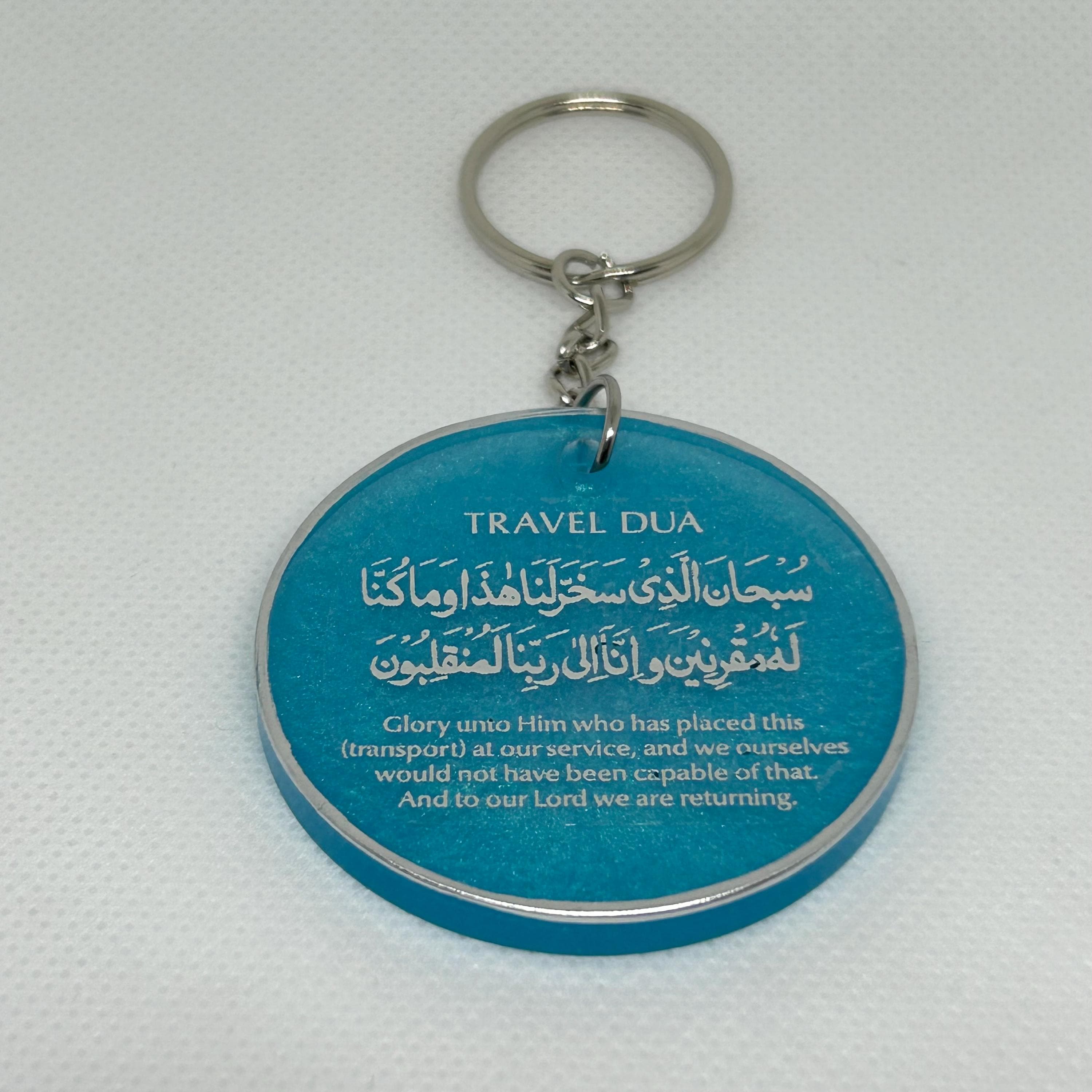 Round 5cm resin keyring in translucent turquoise with the Arabic travel dua with English translation in silver text with a silver edge