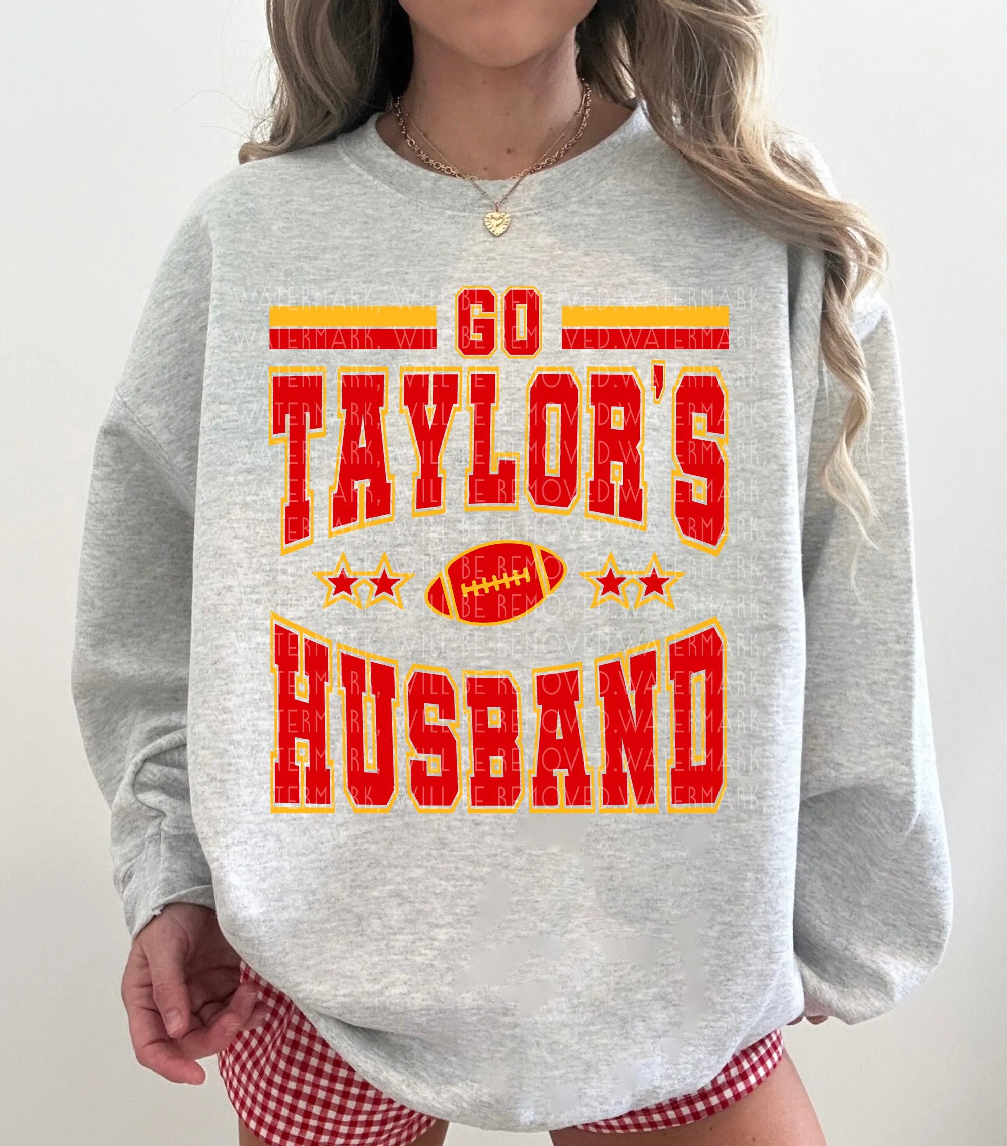 A grey sweatshirt with red and yellow text and graphics, including a football and the text "GO TAYLOR'S HUSBAND".