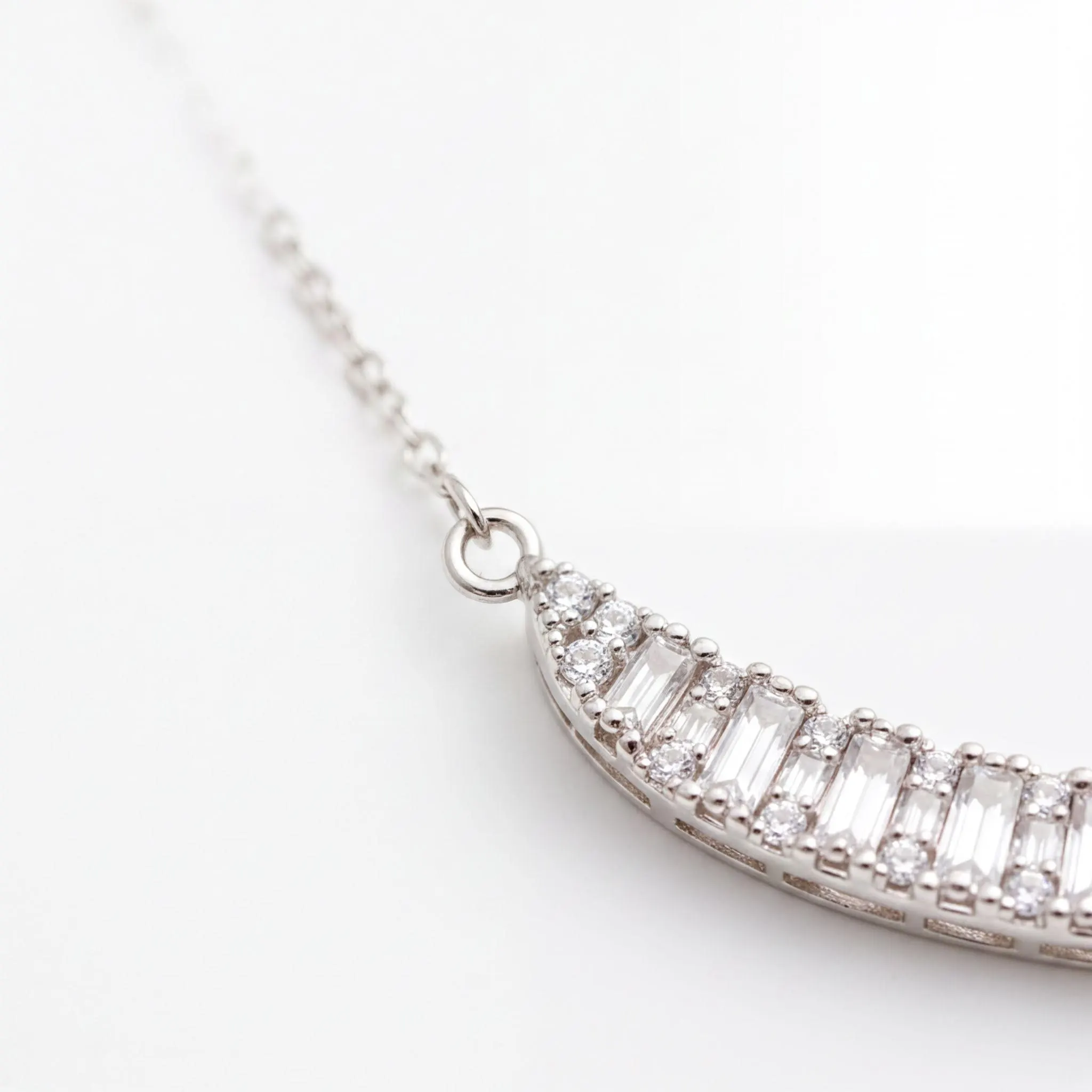 A close-up view of a delicate silver necklace with a row of small, clear diamonds set in the center.