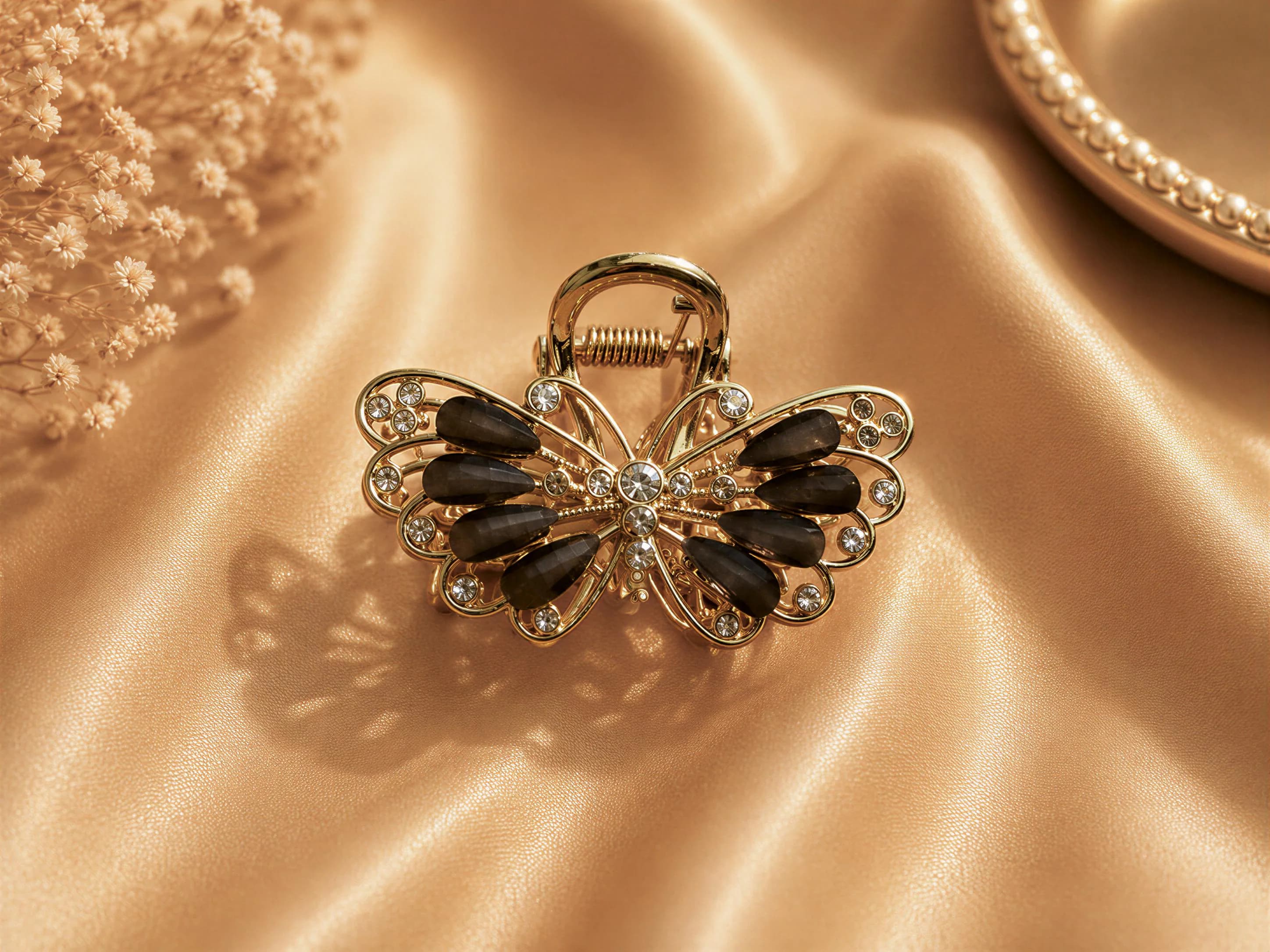 A gold-colored hair clip adorned with black gemstones and a butterfly design rests on a golden fabric surface.