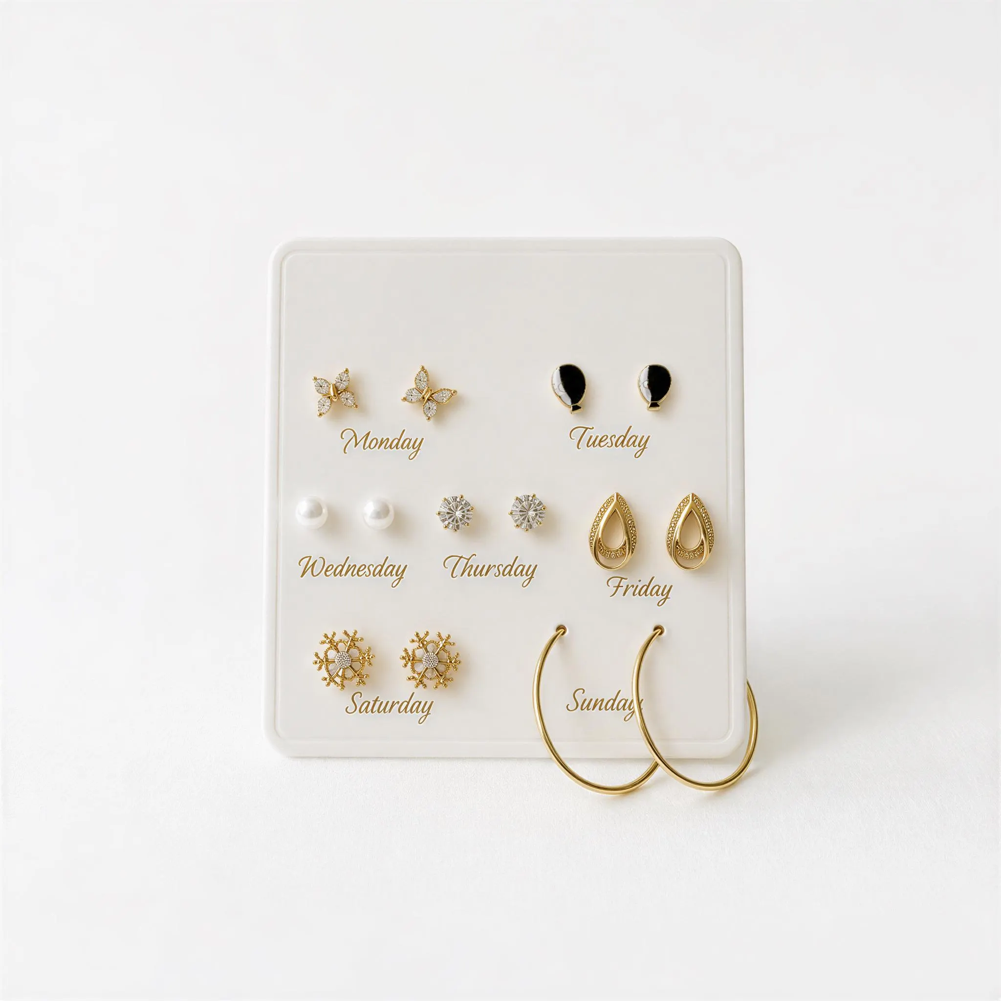 A white jewelry display case containing various gold earrings and earrings, each labeled with the day of the week.