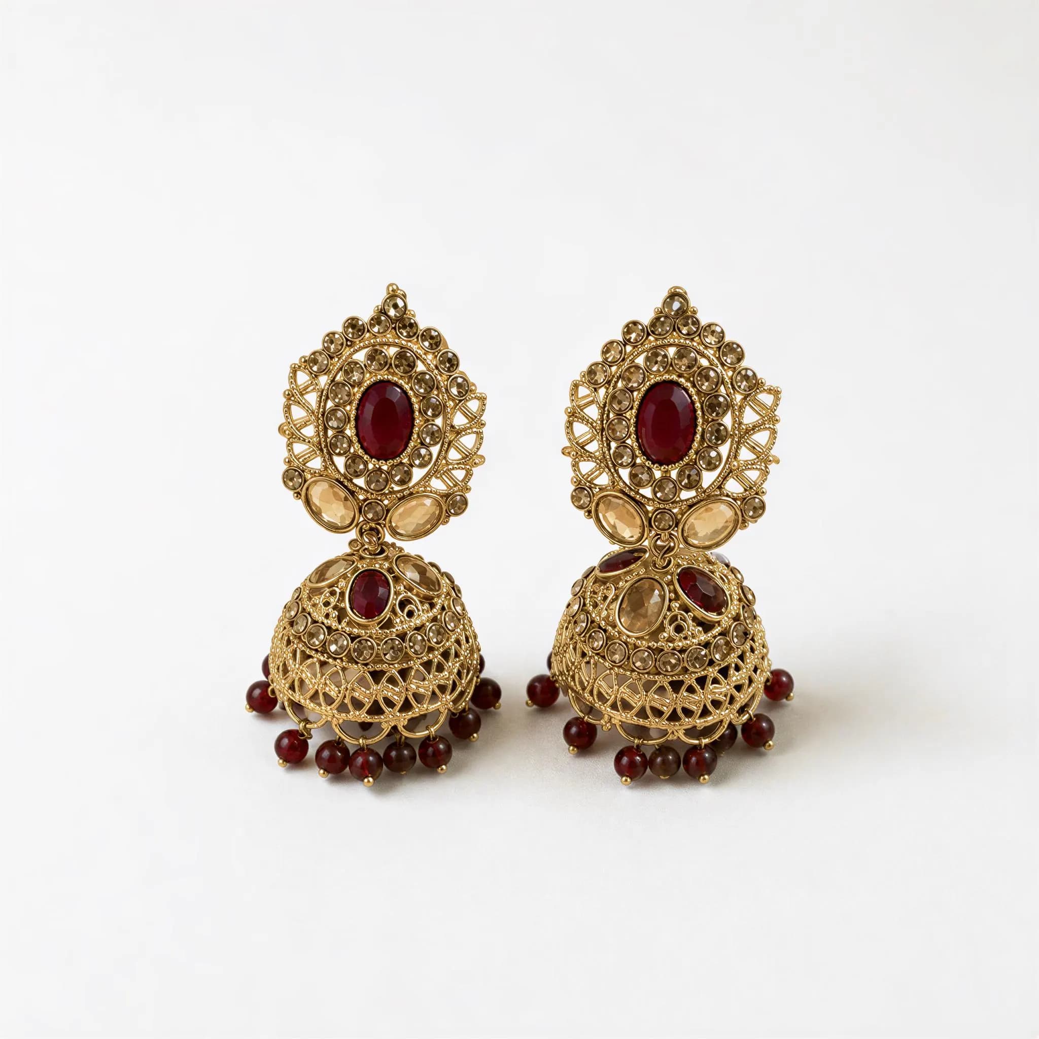 A pair of ornate gold earrings with red gemstones and dangling beads.