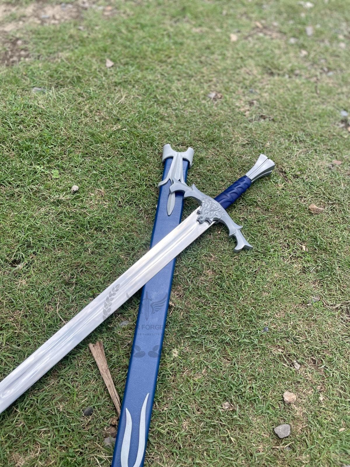 Decorative sword and blue scabbard arranged diagonally across a weathered tree trunk in an outdoor setting.
