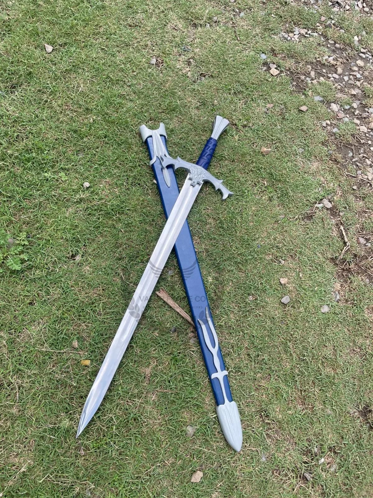 Decorative sword with a blue scabbard placed beside the silver-colored blade on green grass.
