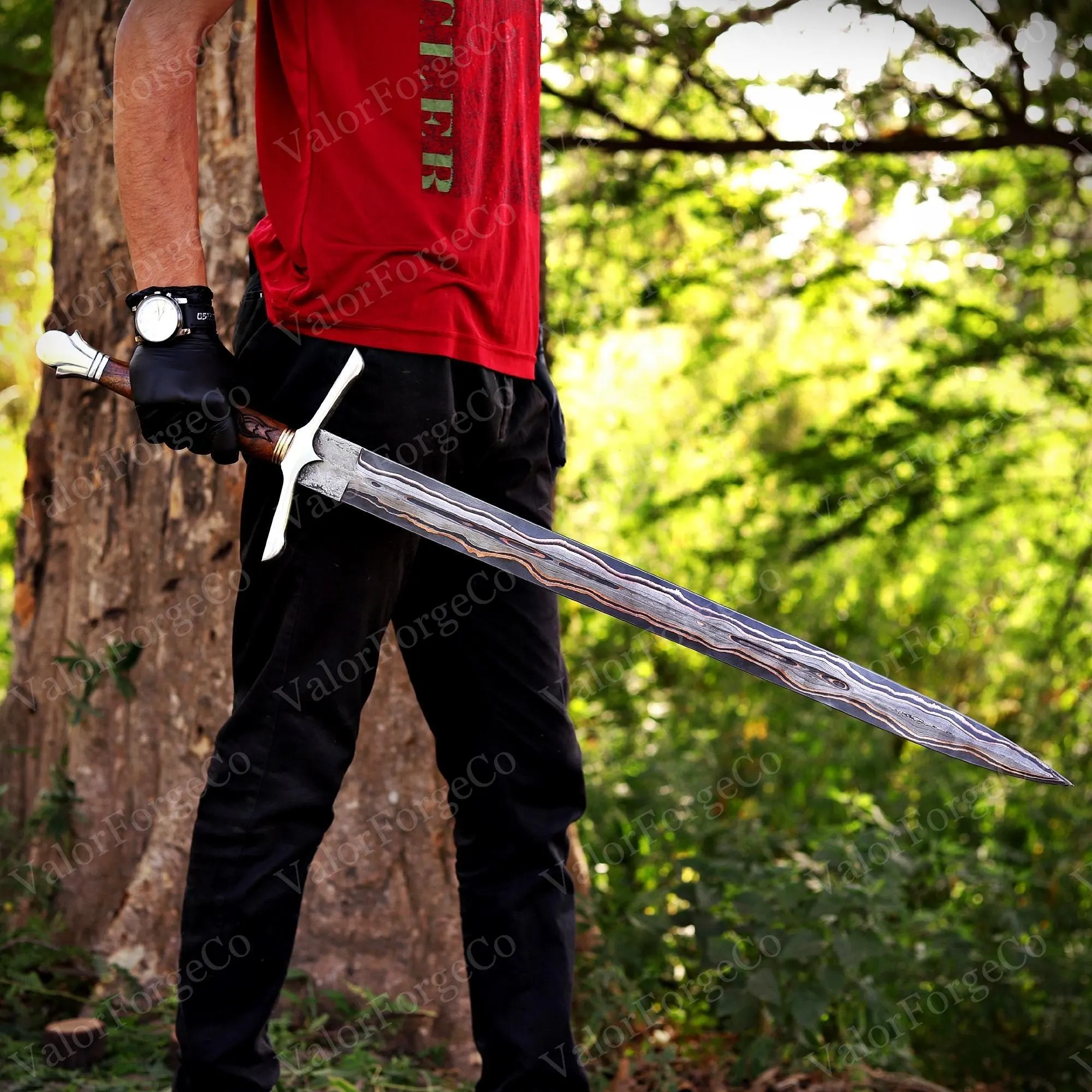 A long sword with a double-edged blade featuring a distinct wavy pattern of layered steel. The hilt includes a silver-coloured crossguard, a dark brown wooden grip, and a white pommel. The blade tapers to a sharp point at the end.