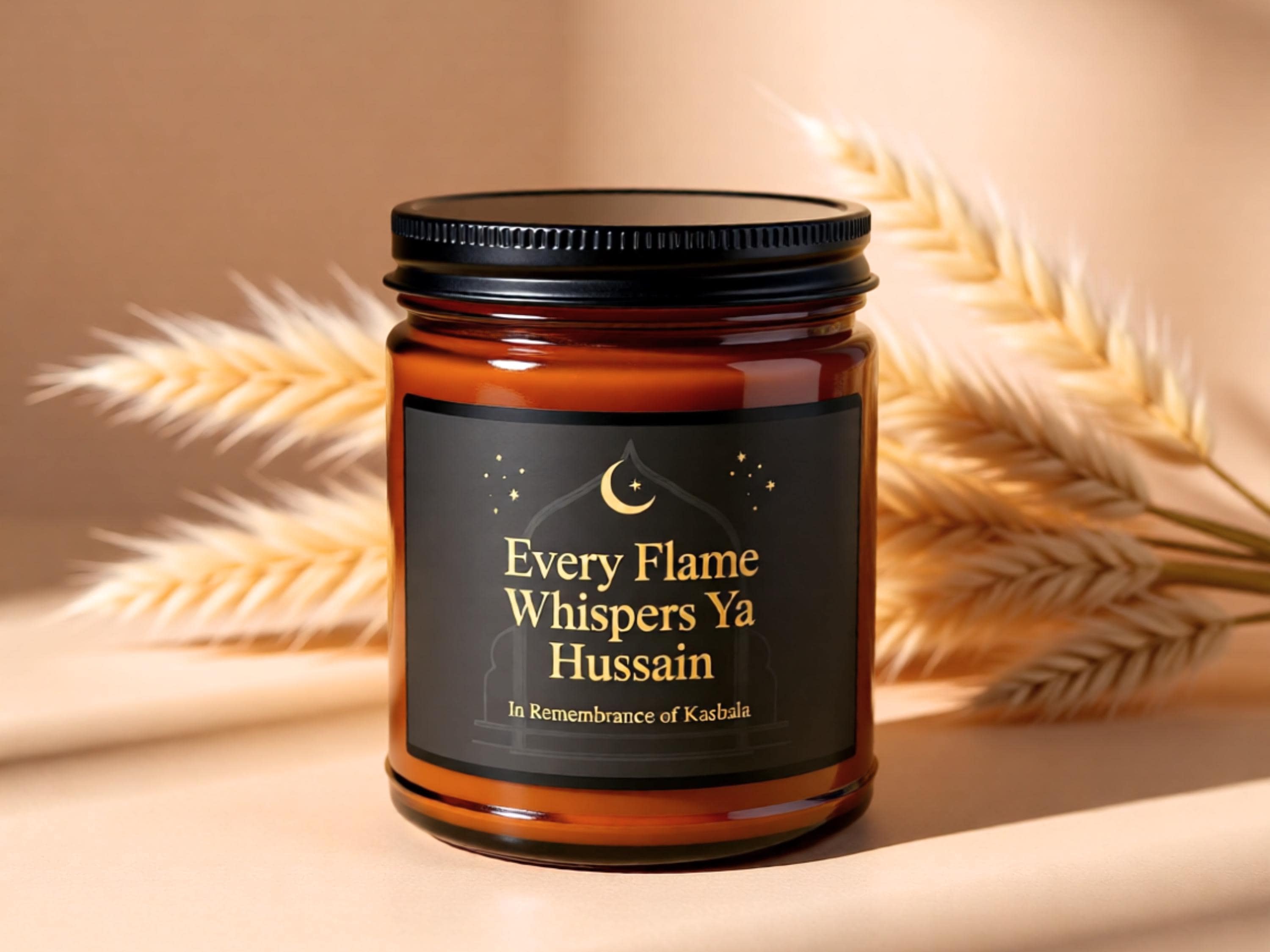 May include: A brown glass jar candle with a black lid and a black label. The label features the text "Every Flame Whispers Ya Hussain" with a crescent moon and stars design. The candle is set against a neutral background with dried wheat stalks.
