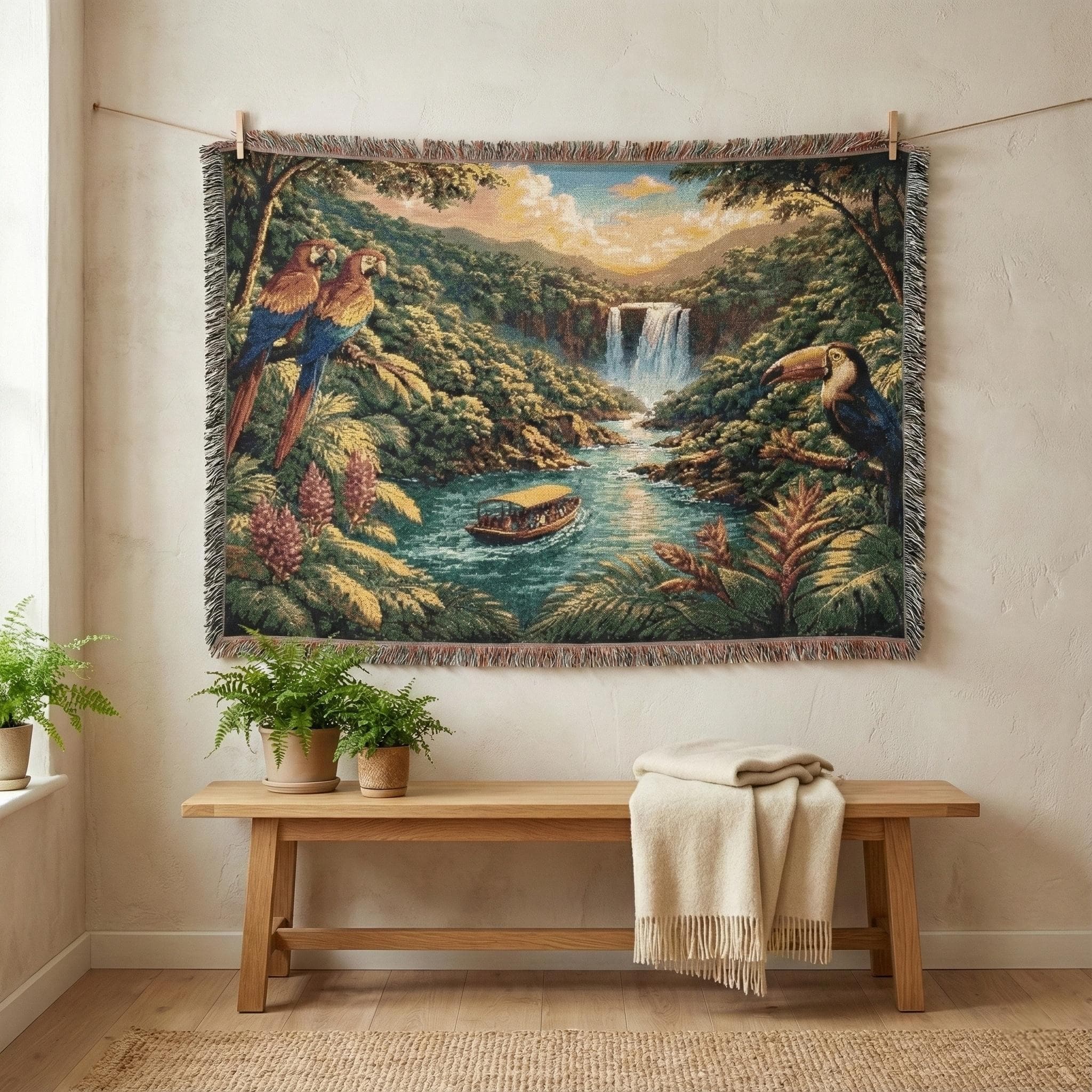 Woven tapestry blanket showing a tropical rainforest landscape with a waterfall in the distance, river flowing through lush green jungle, and a small boat cruising on the water. Colorful parrots perched on the left and a toucan on the right add vibrant wildlife detail. Textured woven look with fringed edges for tapestry wall art, jungle wall decor, coastal tropical home accent, bedroom or living room statement piece. Great gift for nature lovers and bird lovers.