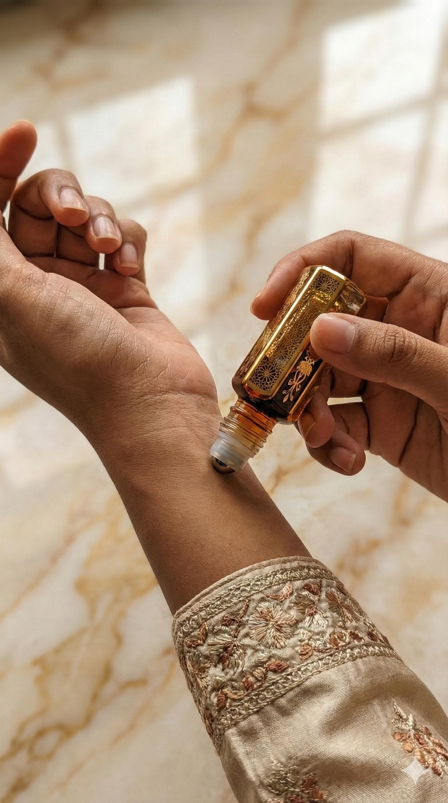 A premium flat-lay ad showing the decorative 11ml attar bottle in its satin-lined case. The bottle is surrounded by fresh green leaves and small, delicate purple patchouli flowers (Pogostemon cablin). Elegant gold typography lists the benefits: alleviating stress, anxiety, and lethargy, while stating it is suitable for both men and women.
