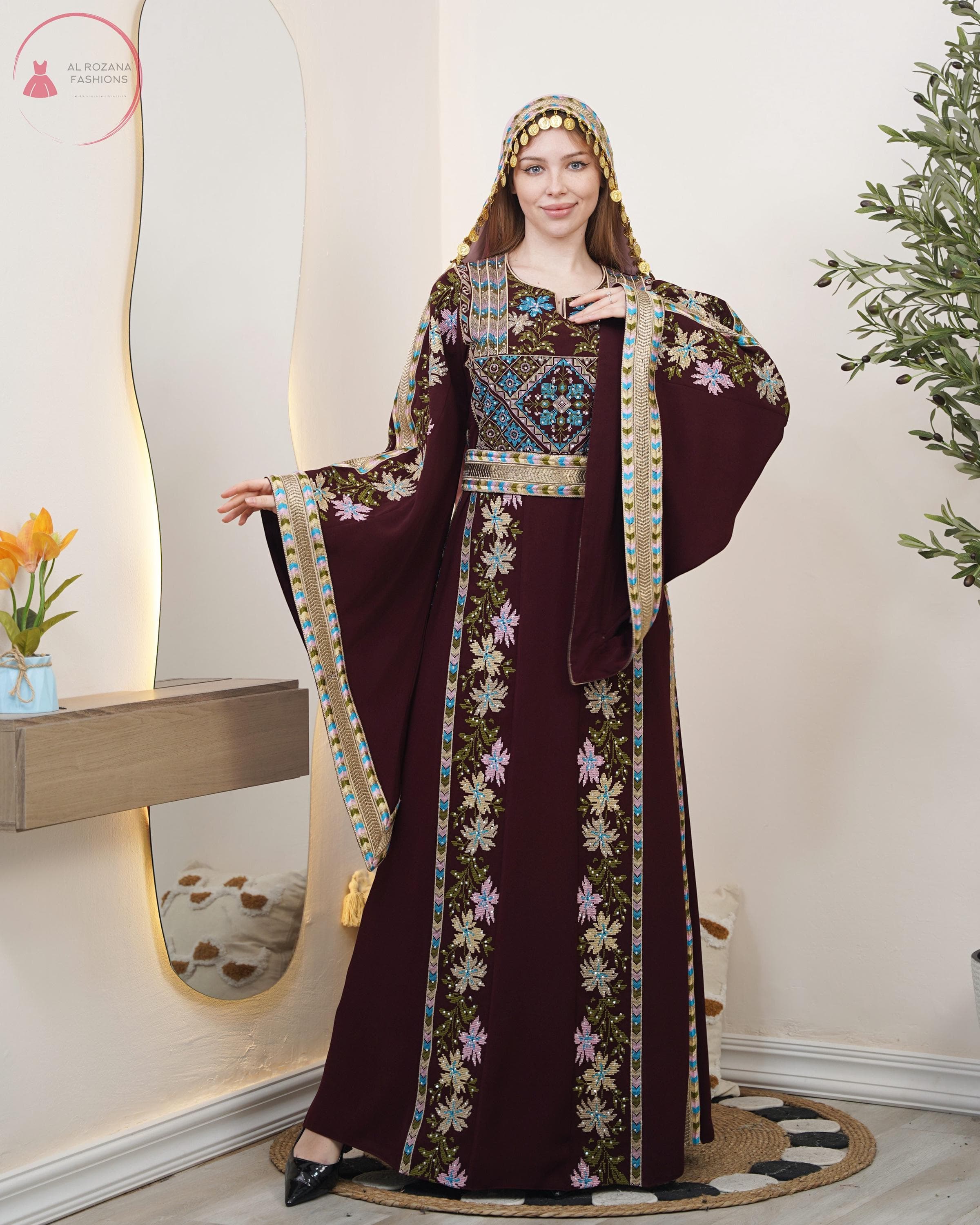 May include: A burgundy dress with intricate floral embroidery and a matching head covering. The dress features long, flowing sleeves and a detailed bodice with geometric patterns. The design includes gold accents and a decorative belt.