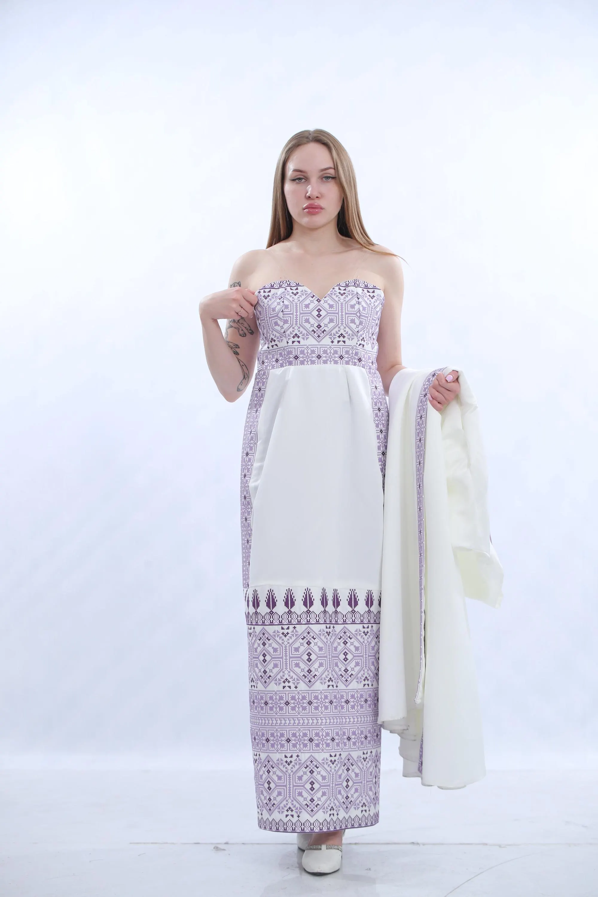 May include: A white formal dress with a long, flowing skirt and a matching jacket. The dress features intricate purple embroidery down the front and on the bodice, creating a striking contrast against the white fabric.