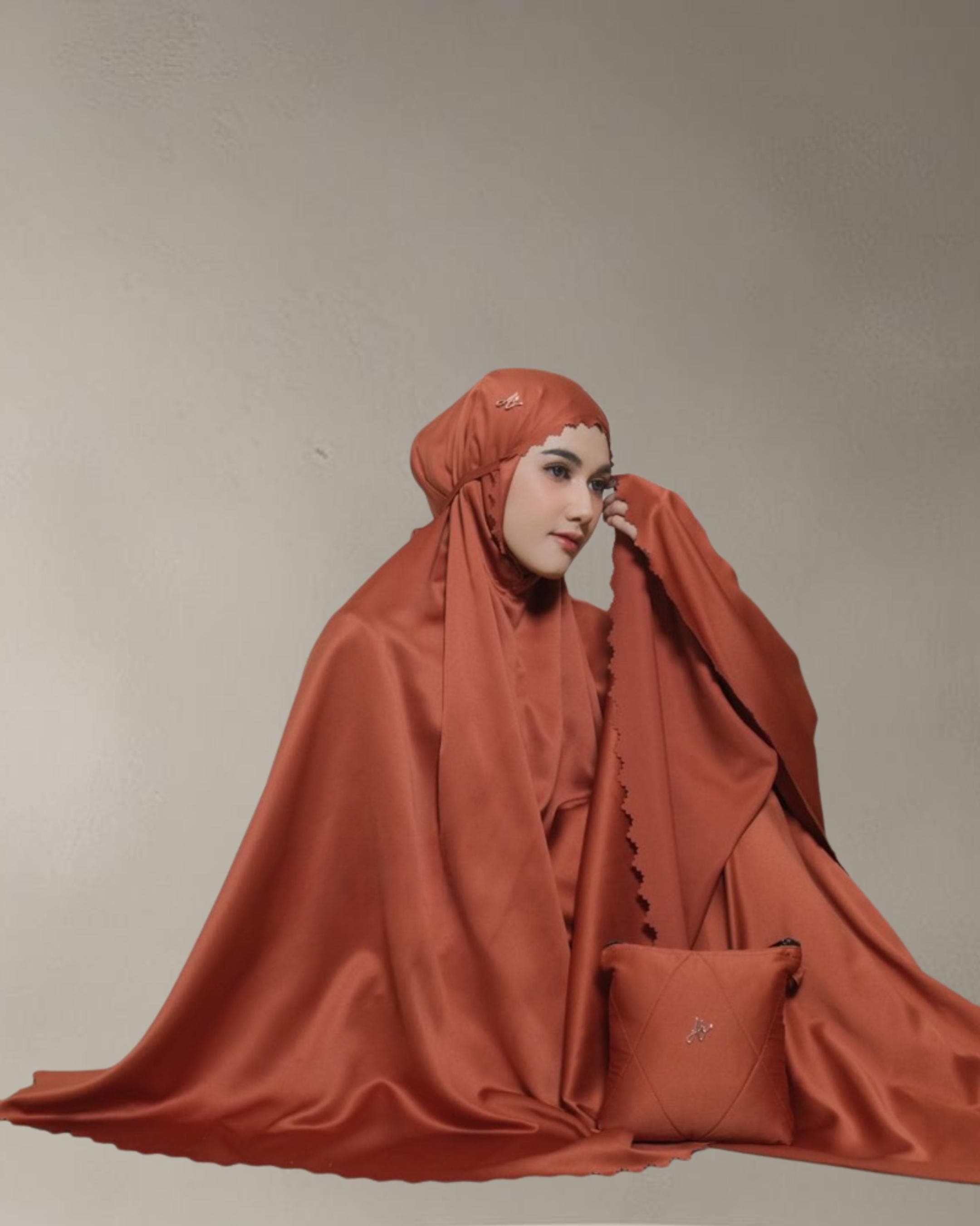 May include: A rust-colored prayer garment set, including a head covering and a matching square bag. The head covering has a scalloped edge and a small decorative embellishment. The set is made of a smooth, satin-like fabric.