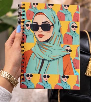 May include: Spiral-bound notebook featuring a stylized illustration of a woman wearing a teal hijab and sunglasses. The design is repeated in horizontal rows against a yellow background. The notebook is held by a person with a gold watch and blue nail polish.