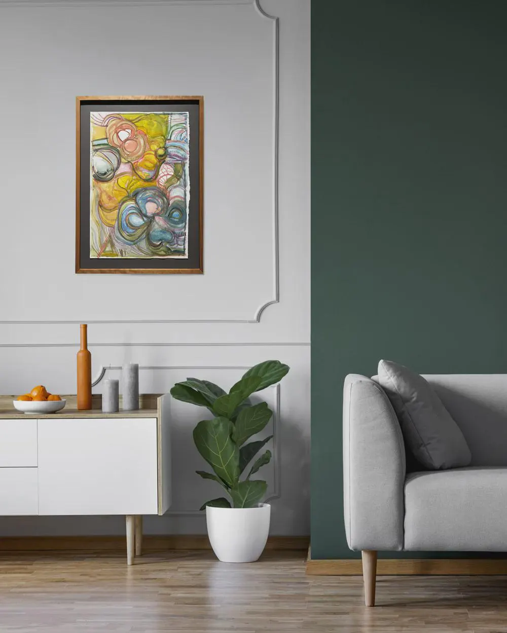 May include: Abstract watercolor painting in a wooden frame. The artwork features colorful, swirling shapes in shades of yellow, blue, and pink. The painting is displayed on a gray wall above a white cabinet with a plant and a sofa.