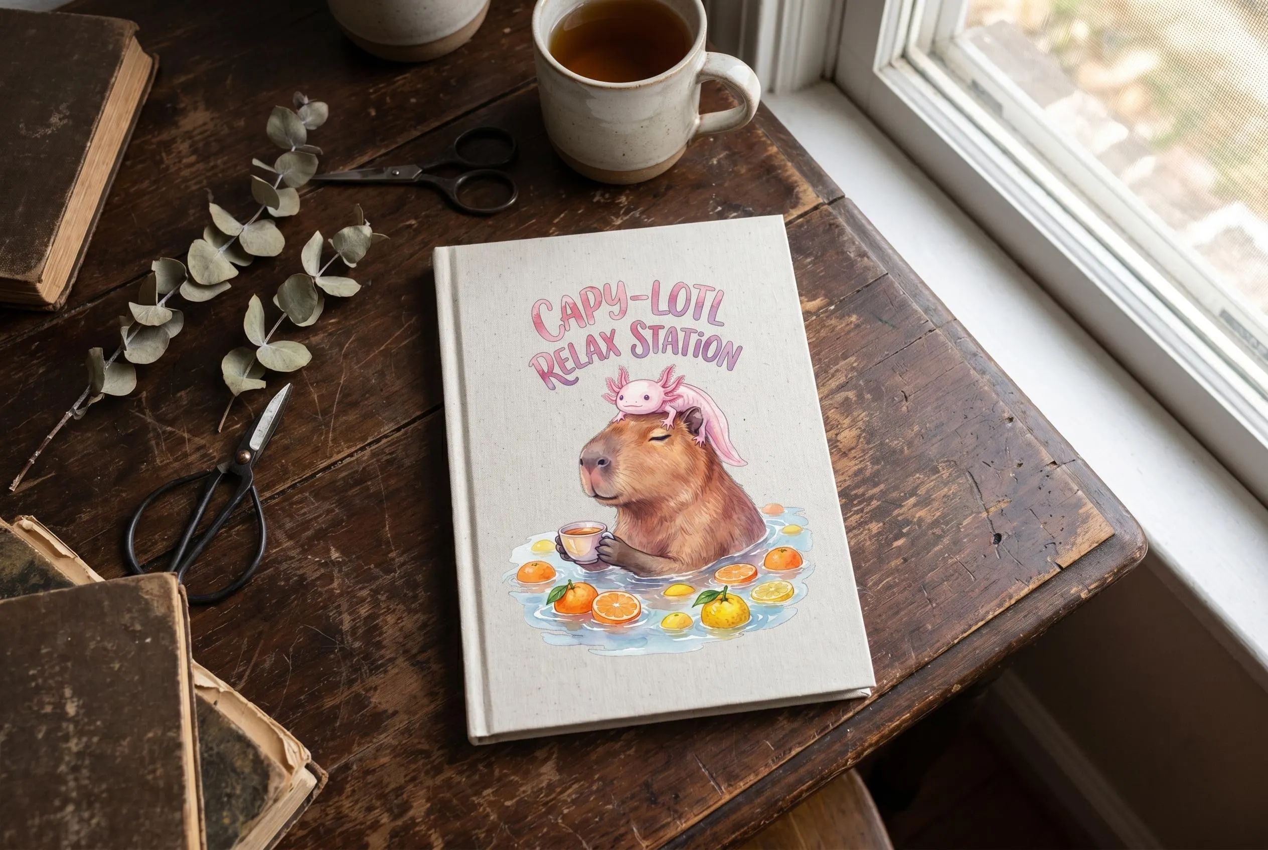 Notebook with Capybara Axolotl PNG — cute watercolor capybara soaking in a citrus bath with oranges and lemons, holding a tea cup, pink axolotl resting on its head, "Capy-Lotl Relax Station" pink arch text above. Funny capybara designs axolotl clipart placement example.