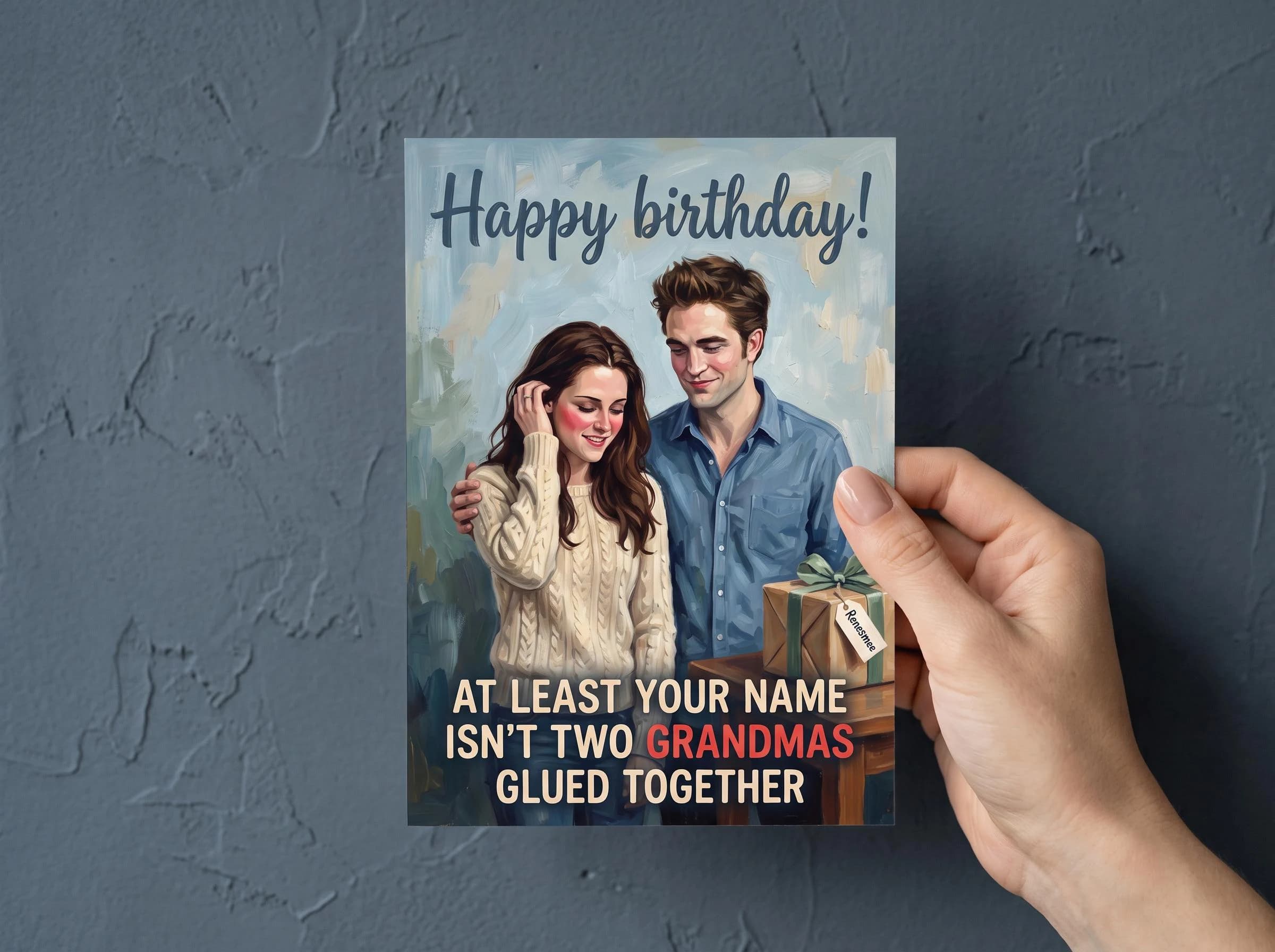 Funny birthday card printed and ready to give: a blushing Bella Swan in a cream knit sweater and a smiling Edward Cullen in a blue shirt stand beside a present tagged Renesmee. Caption: Happy birthday! At least your name isn't two grandmas glued together. A Twilight card and funny quote for a 25th birthday, 30th birthday or any fan of the saga.