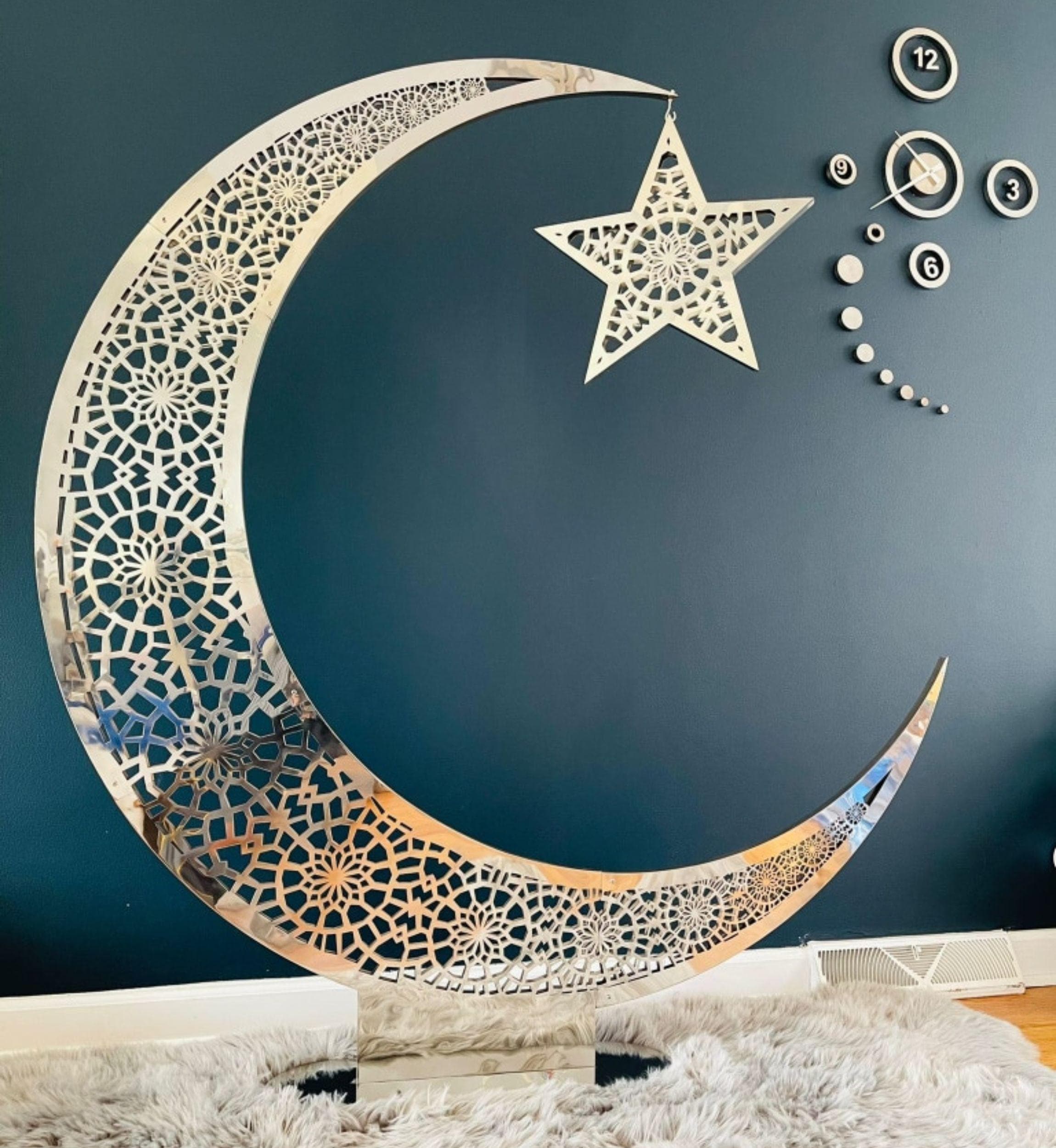 A large, freestanding silver crescent moon with intricate cut-out patterns, holding a matching star by a chain, stands on a flat base.