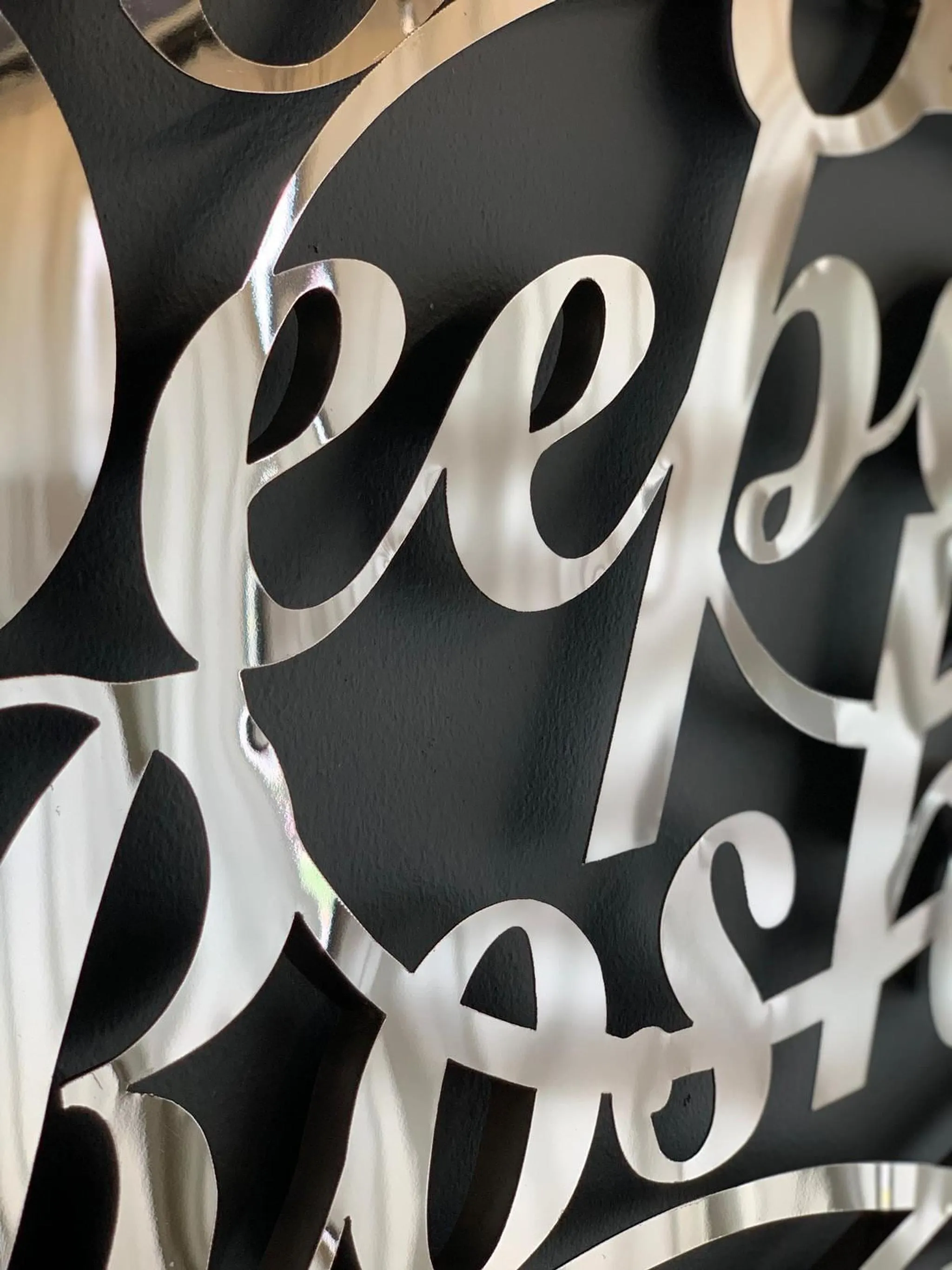 A close-up view showing the shiny, polished metallic surface of the cursive letters on the custom wall sign.