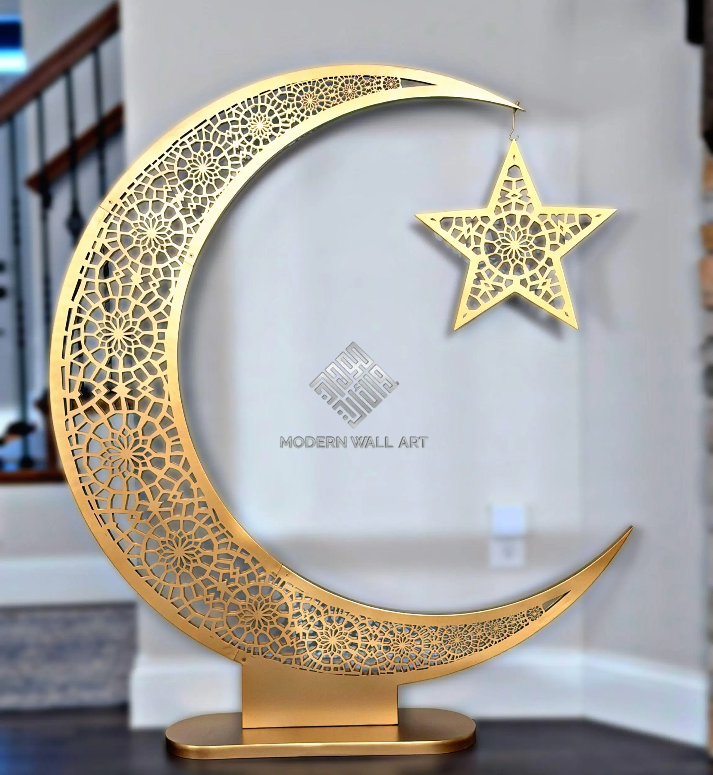 A large, freestanding golden crescent moon with intricate cut-out patterns, holding a matching star by a chain, stands on a flat base.
