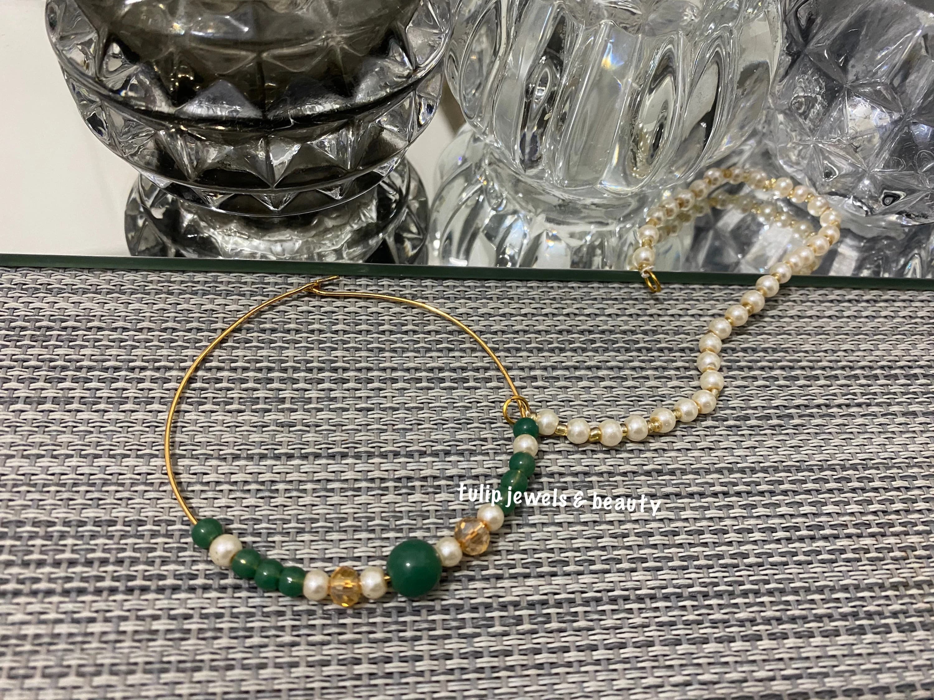 Gold hoop nose ring with green and white beads. The ring is attached to a string of white pearls.
