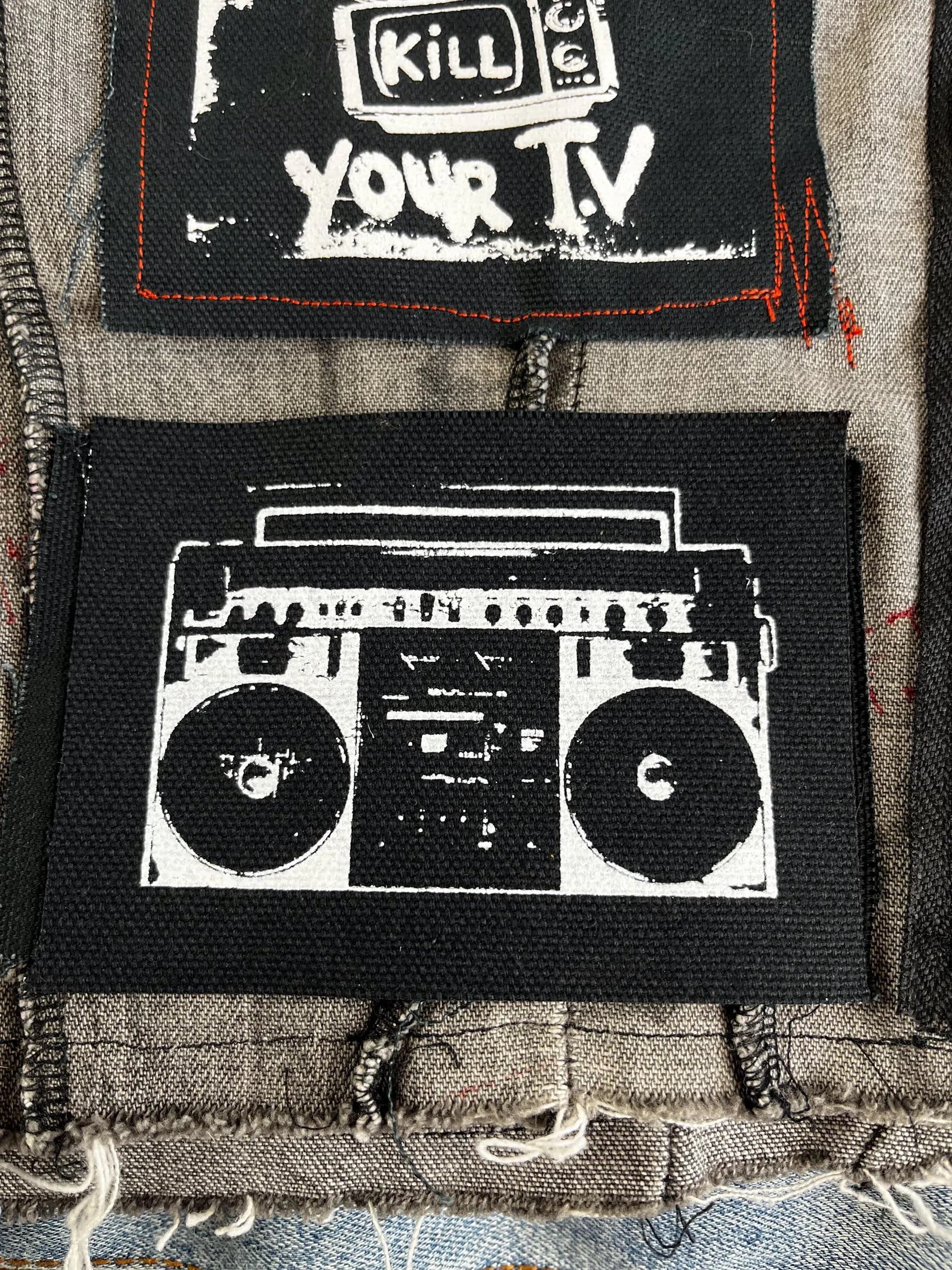 Boombox punk patch sewn onto a denim battle vest with other DIY patches and punk accessories.