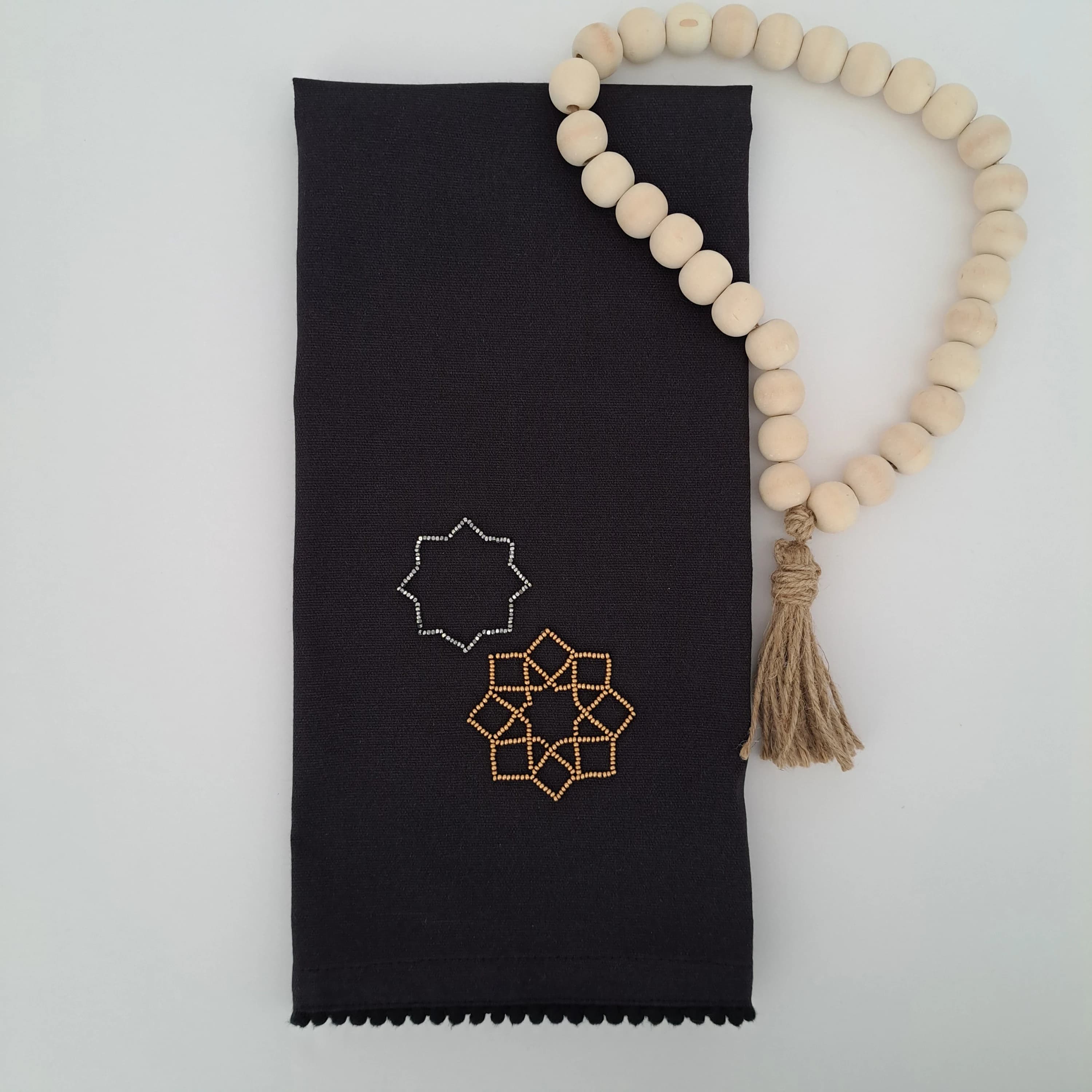islamic geometry star design in silver and gold beads. on a black tea towel