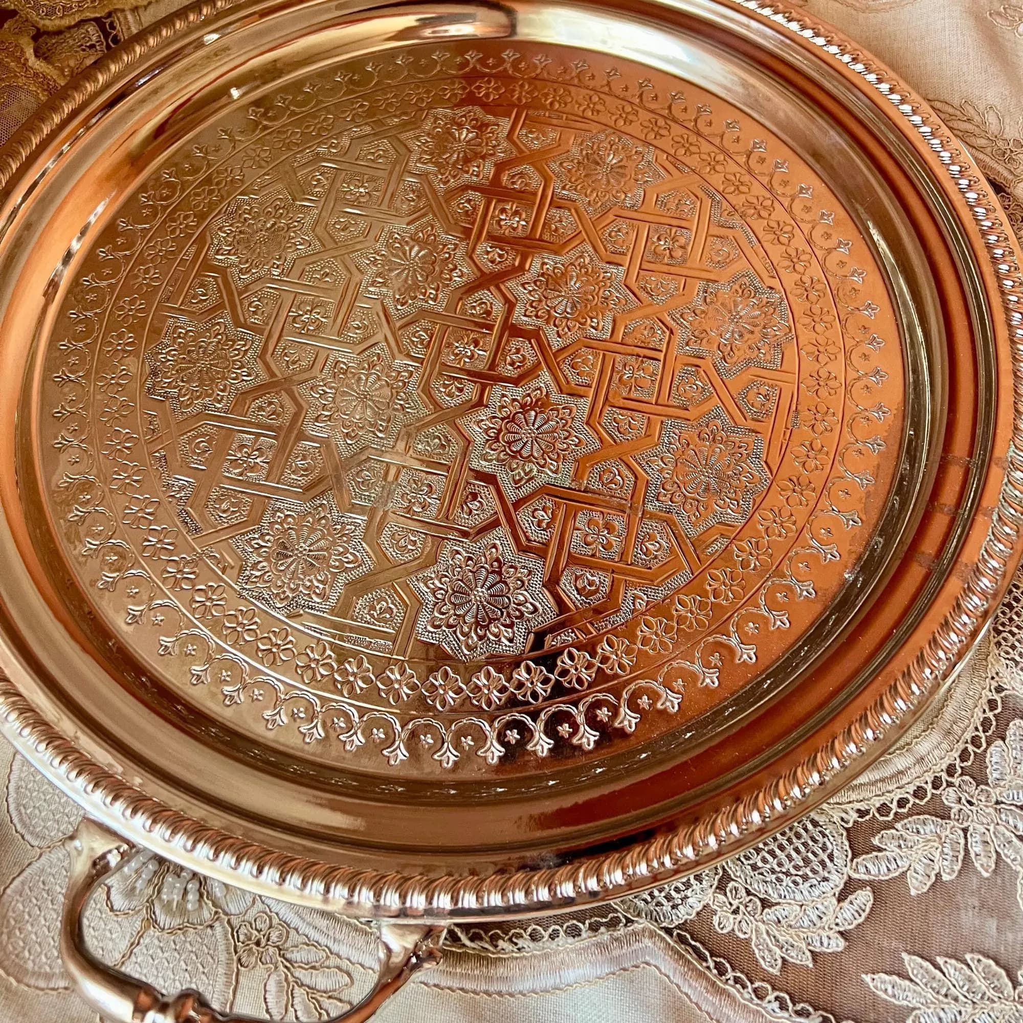 A close-up view of the intricate geometric and floral engraved pattern on the round silver serving tray.
