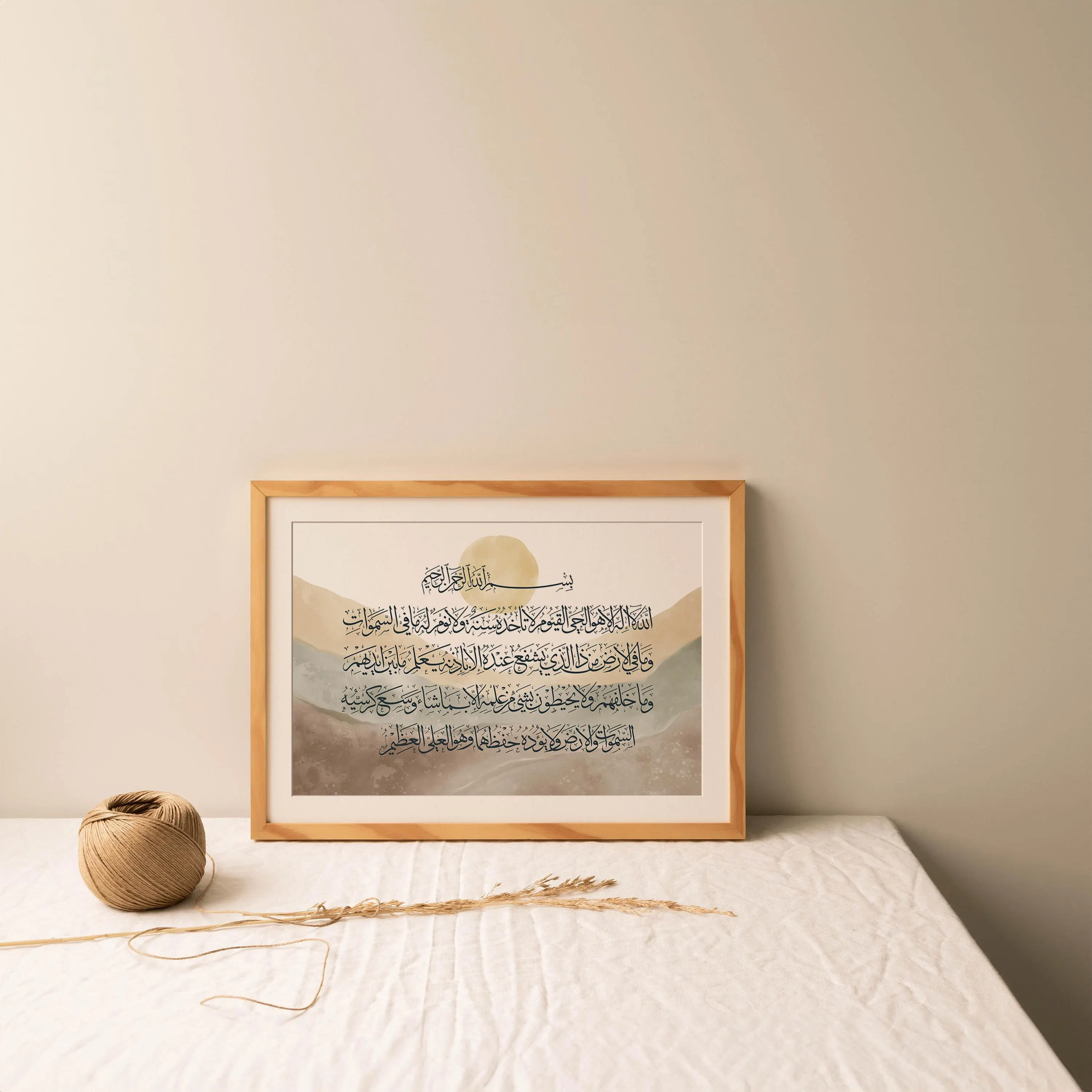 Islamic calligraphy print of Ayat al-Kursi framed in wood, styled on a linen-covered table with twine and dried grass, warm lighting creating a cozy, bohemian atmosphere.