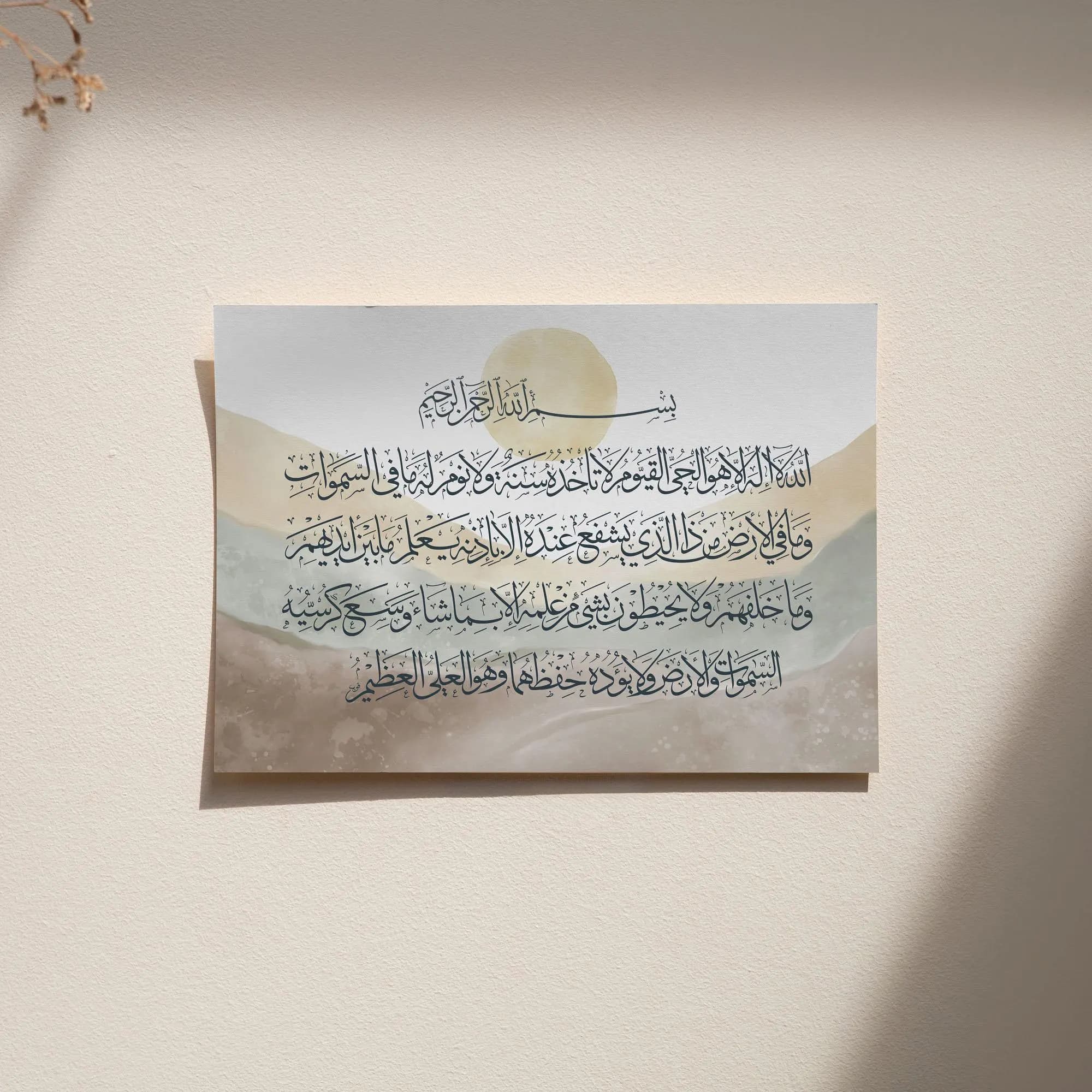 Minimalist Ayat al-Kursi print with Arabic calligraphy in black ink over watercolor mountains in beige and green hues, sunlight highlighting the paper pinned flat against a neutral wall.