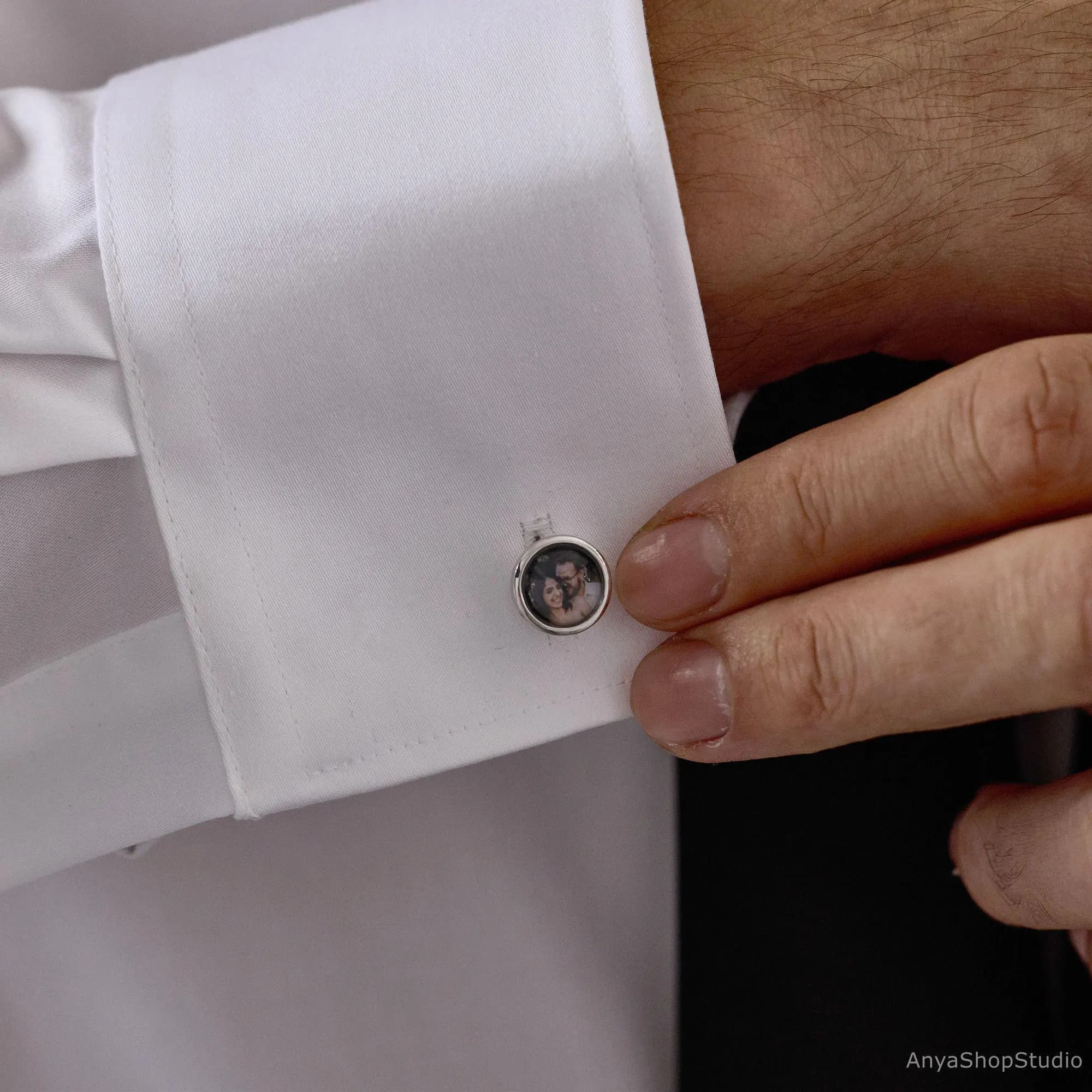 May include: Silver cufflinks with a personalised photo. The cufflinks are round and feature a small, framed image. The image is of a couple. The cufflinks are attached to a white dress shirt.
