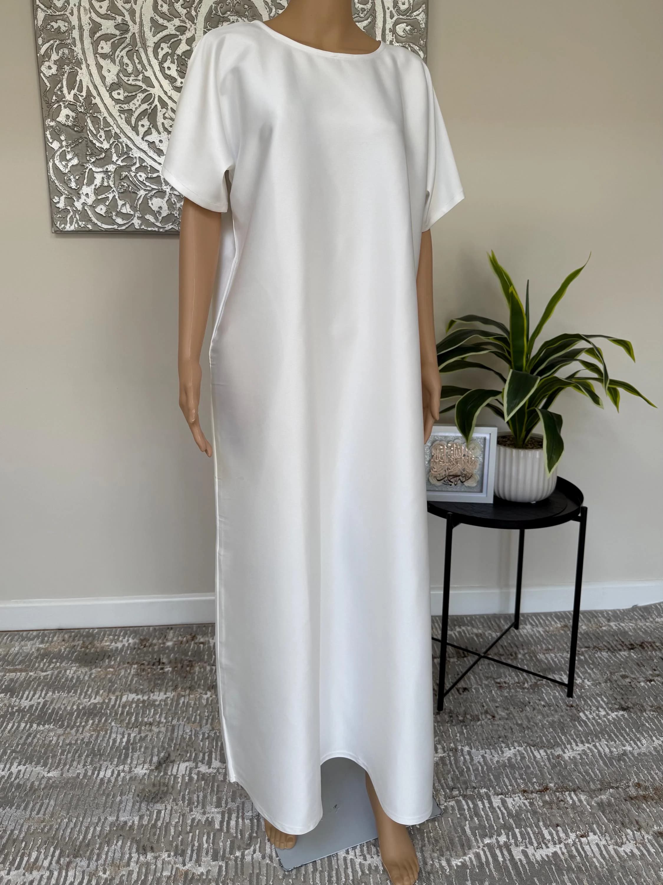 May include: A long, white dress with short sleeves. The dress features a simple, elegant design and a round neckline. The fabric appears smooth and flowing. The dress is displayed on a mannequin.