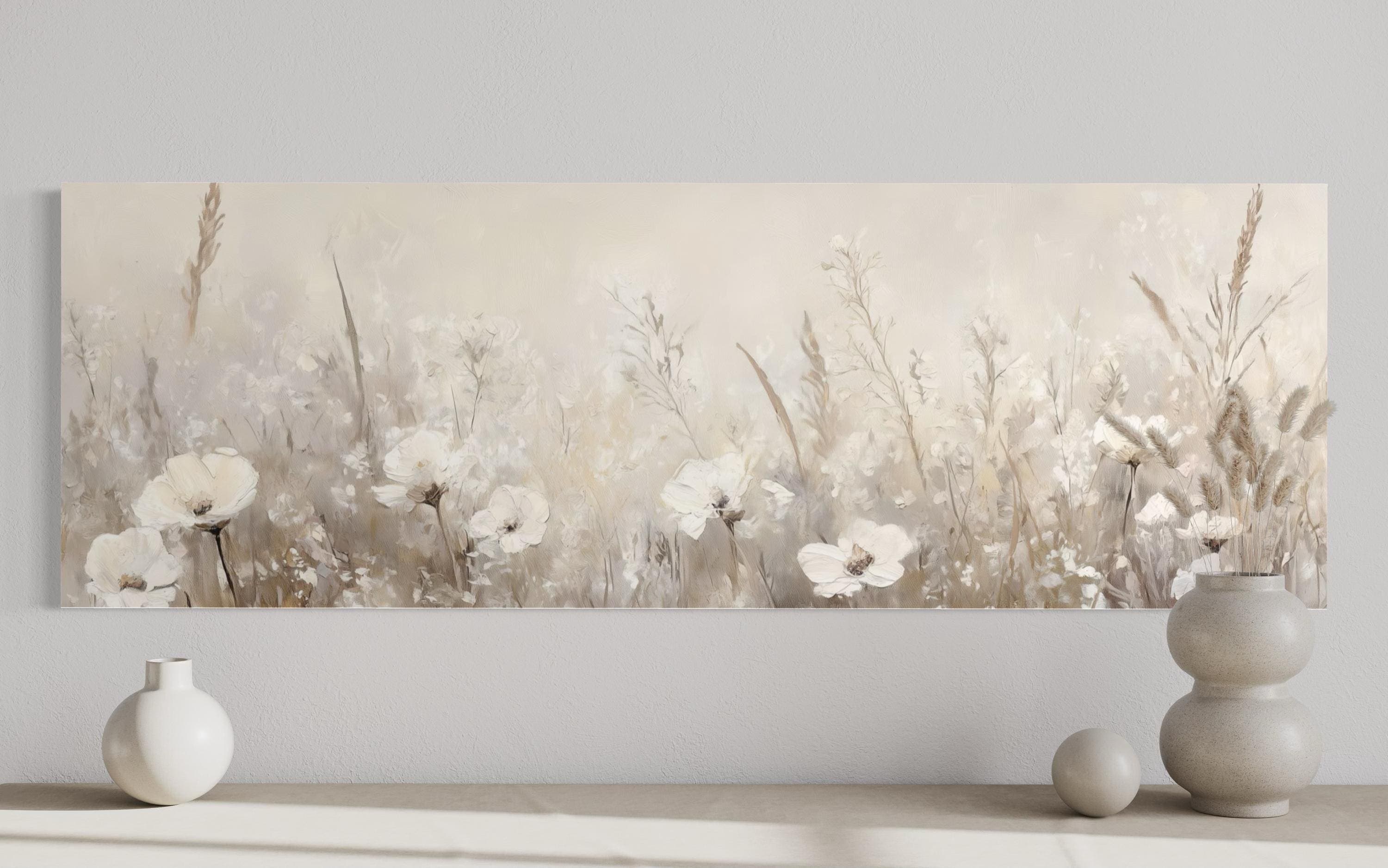a large painting of a field of white flowers on a wall, with two white vases placed on a shelf below it.