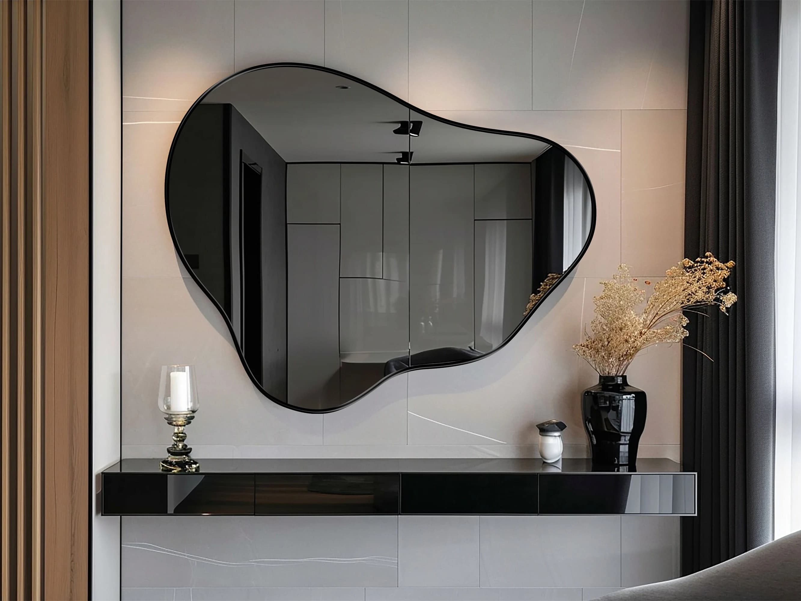 Organic Pebble Mirror with black frame finish hung on the wall of a living room, over a shelf.