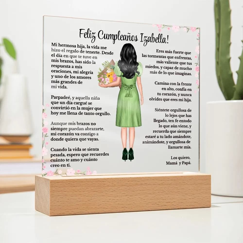 May Include: A personalized acrylic plaque displayed on a wooden LED base in a home setting. The custom design features a birthday message, pink floral accents, and an illustrated girl with long black hair wearing a green dress and holding a bouquet. A cactus and decorative vase are blurred in the background.