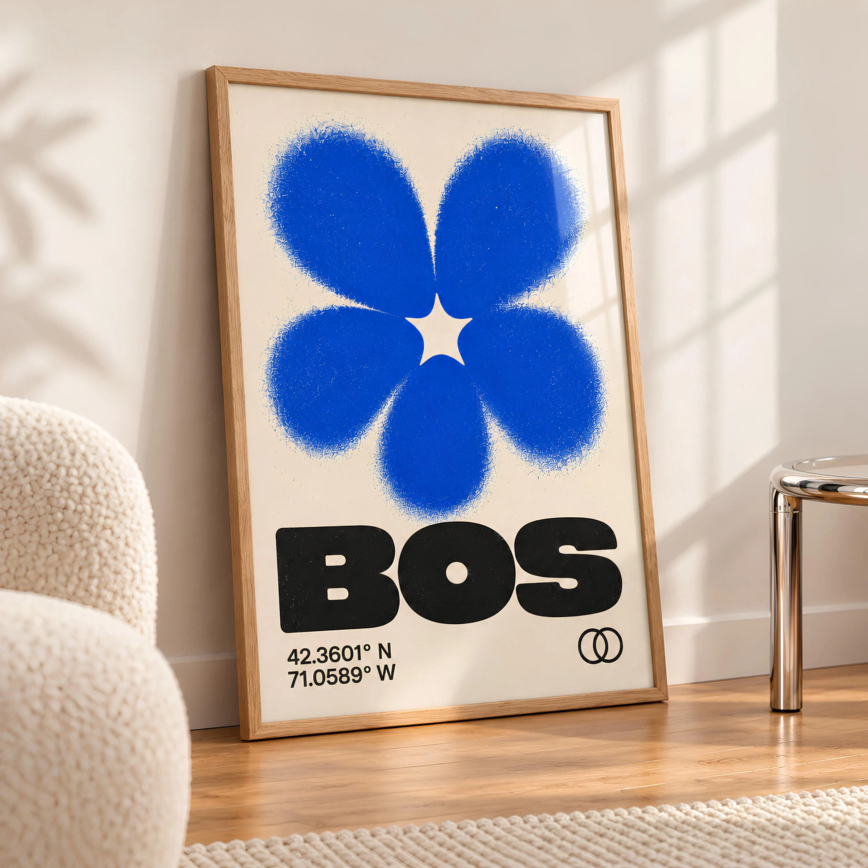 A framed vertical wall art print featuring a large, vibrant blue flower graphic with a textured, spray-paint effect. Below the flower, the text BOS is printed in bold black letters, followed by the coordinates 42.3601 N 71.0589 W.