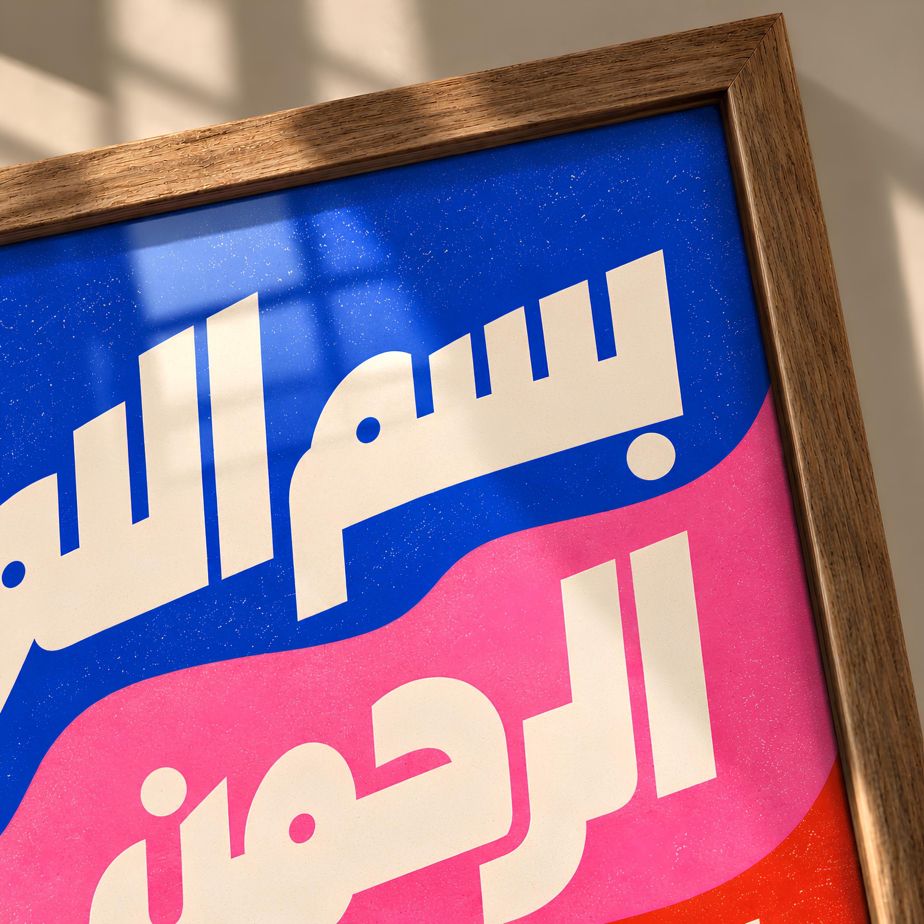 A framed wall art print featuring bold white Arabic calligraphy against wavy, layered background sections of vibrant blue, bright pink, and orange. The text reads Bismillah Ar-Rahman Ar-Rahim. The frame is made of light brown wood.