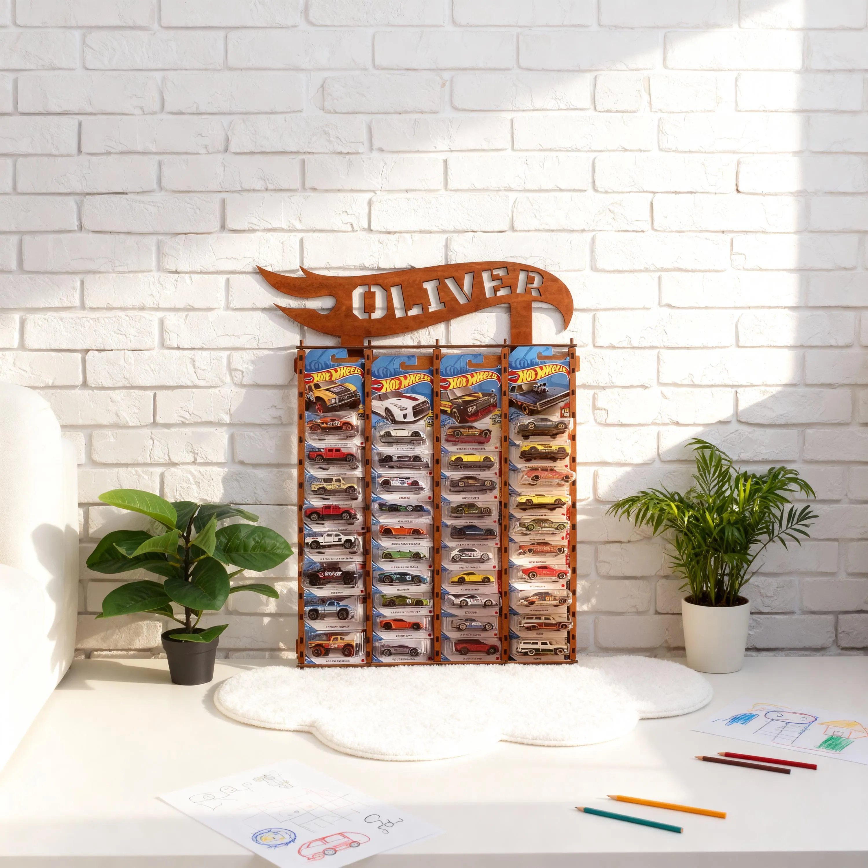 May include: A wooden Hot Wheels car display rack with the name "OLIVER" cut out at the top. The rack is filled with various Hot Wheels cars in their original packaging. The display is set against a white brick wall.