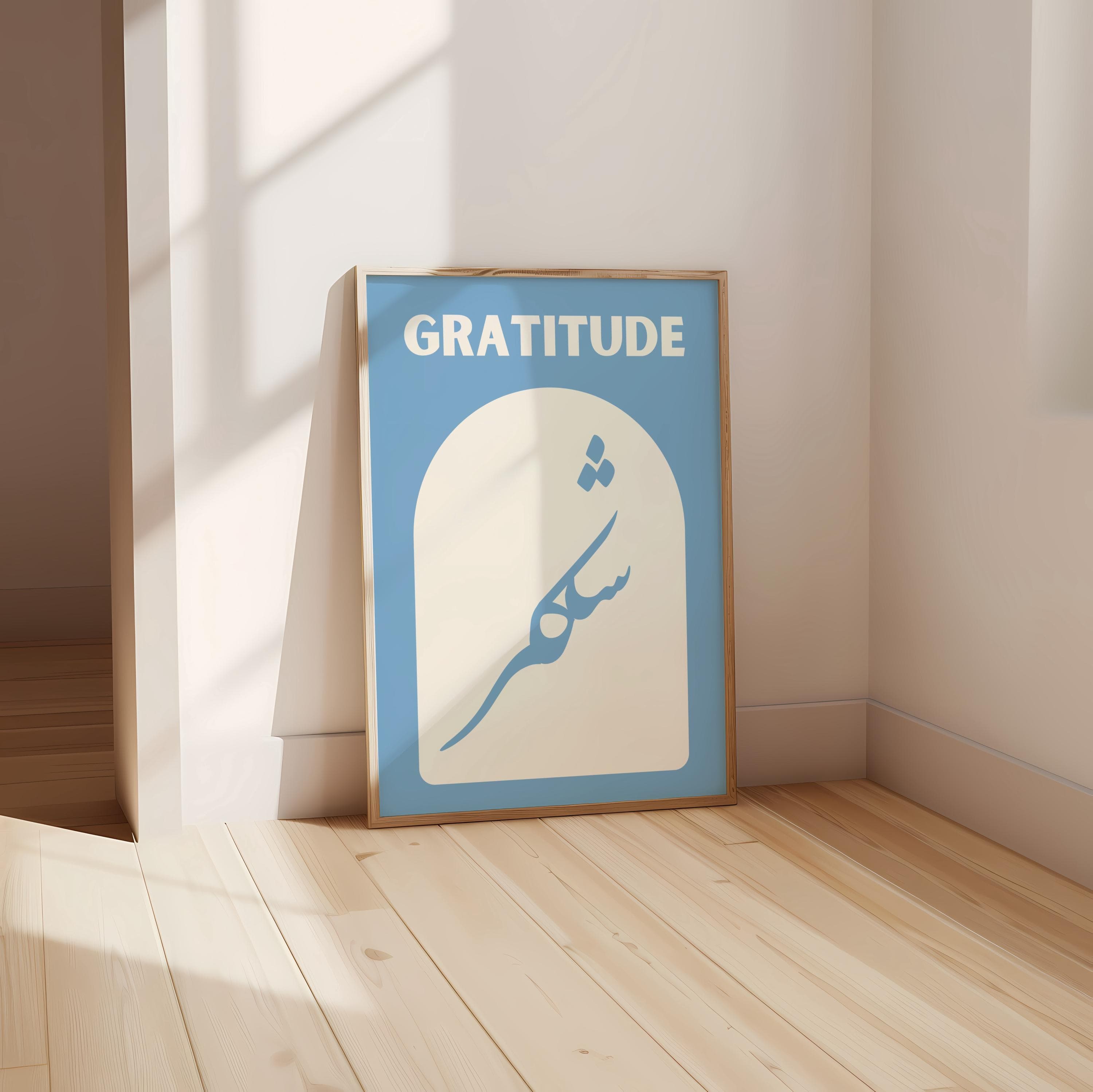 The artwork features a soft blue background featuring the word "GRATITUDE" in bold light beige letters at the top and the Arabic word for gratitude, "shukr" written elegantly below, inside an arched shape.