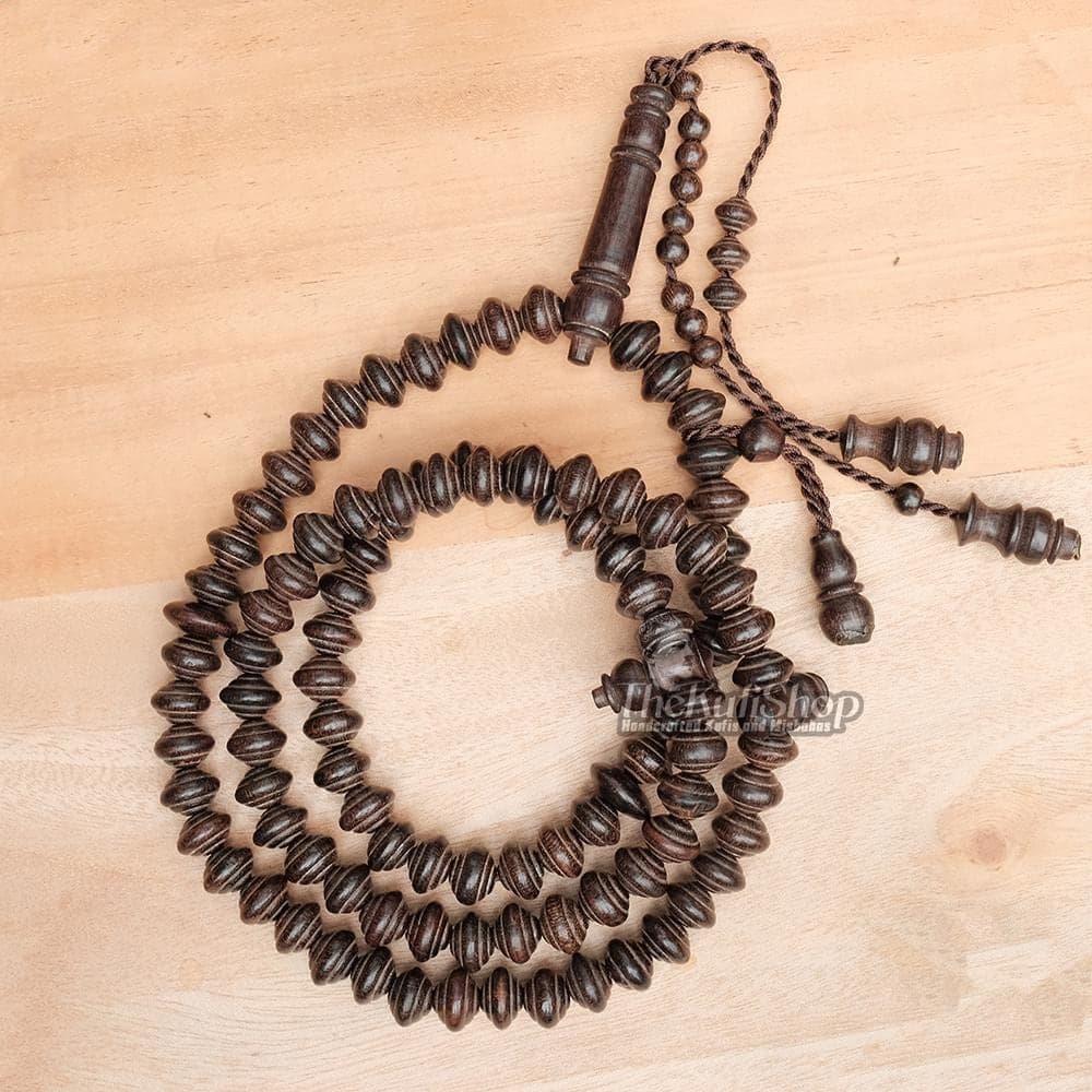 Dark brown 8x11 mm saucer-shaped beads Tamarindwood tasbih with 99 beads. The Tasbih includes a beautifully carved imam/alif bead and an adjustable tension design for comfortable. Tasbih is rolled up and placed on a flat wooden plank