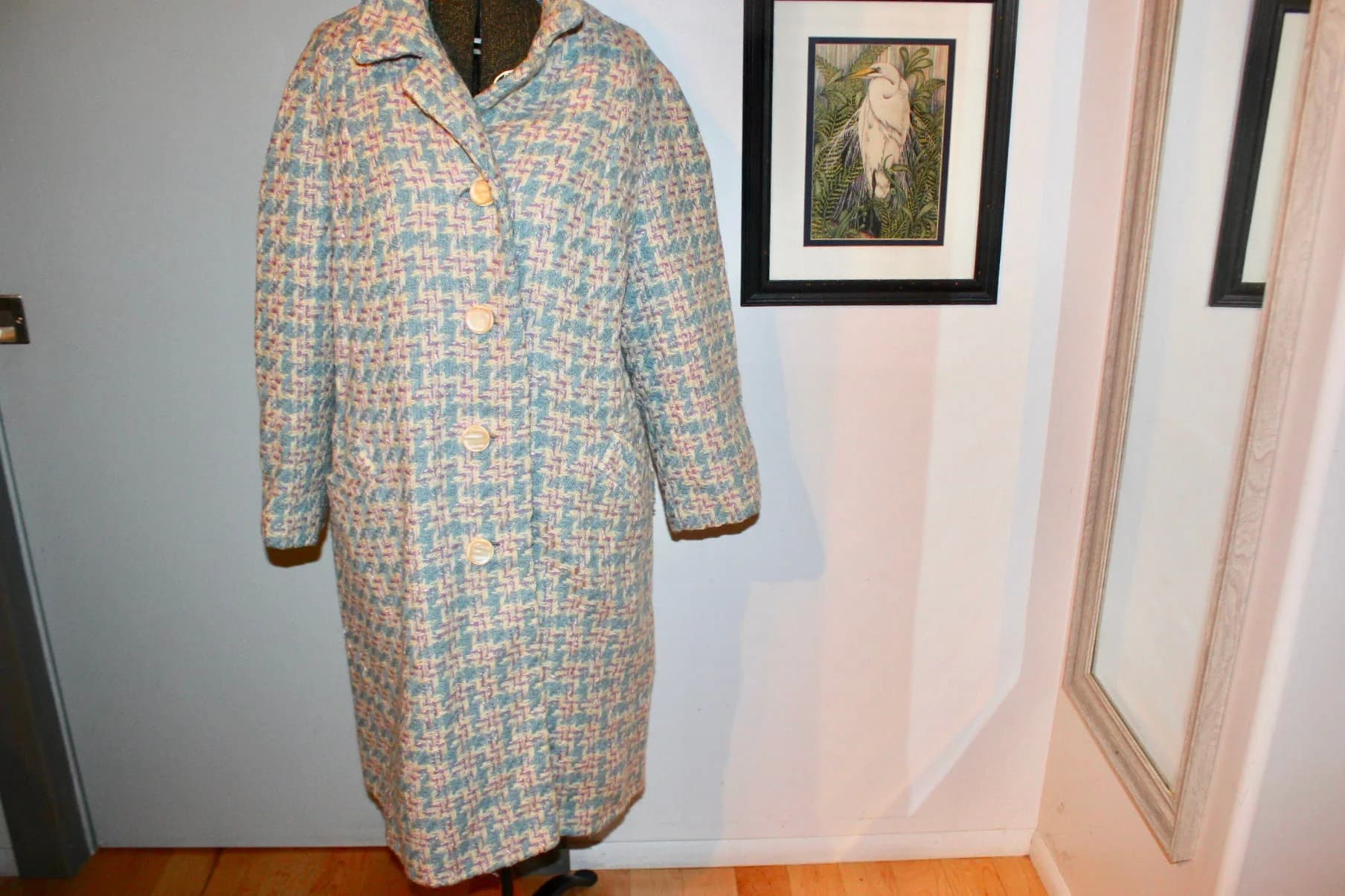 May include: A vintage, knee-length coat in a blue, beige, and red houndstooth pattern. The coat features a notched collar, three large beige buttons, and two front pockets. It is displayed on a dress form.