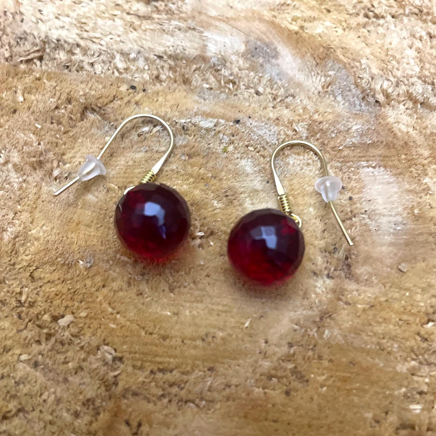 Polished red amber gemstone earrings, round faceted drops with gold ear hooks, lightweight handmade jewelry design.