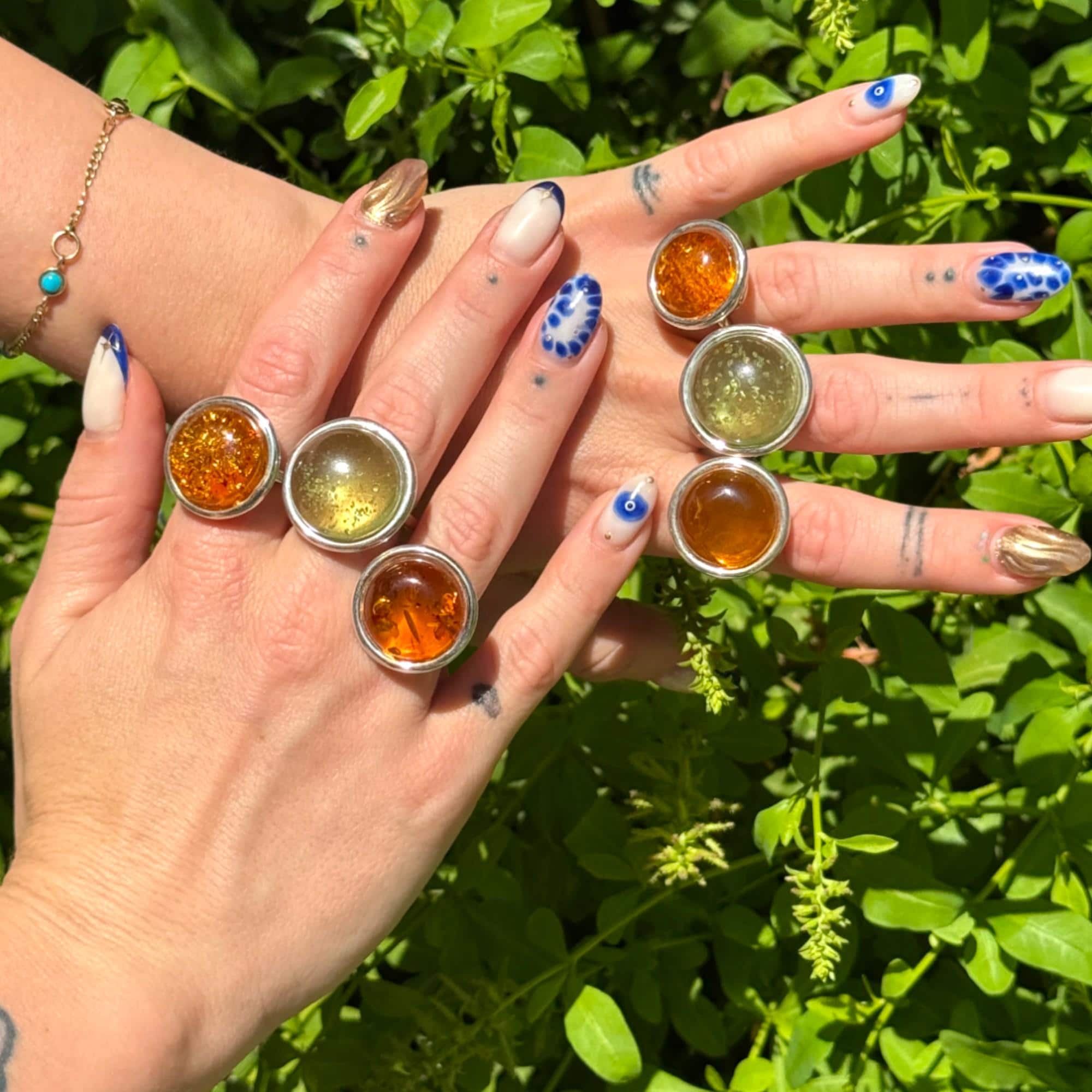 Collection of adjustable silver rings showcasing polished green and honey amber gemstones, each uniquely set