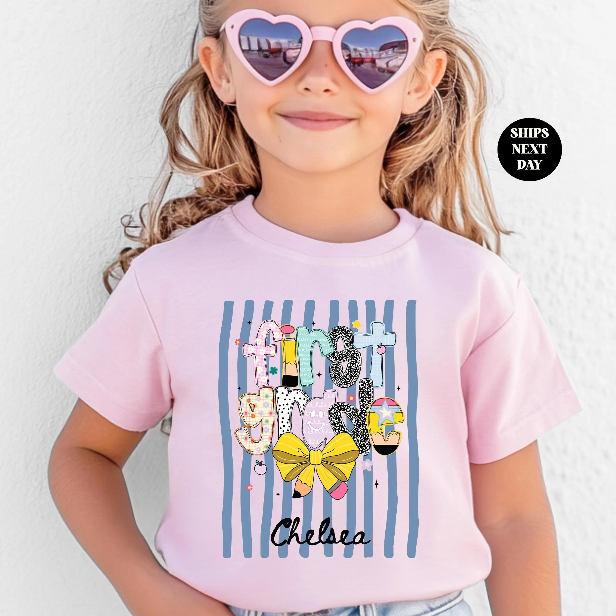 A young girl wearing a pink t-shirt with a graphic design and sunglasses, smiling at the camera.