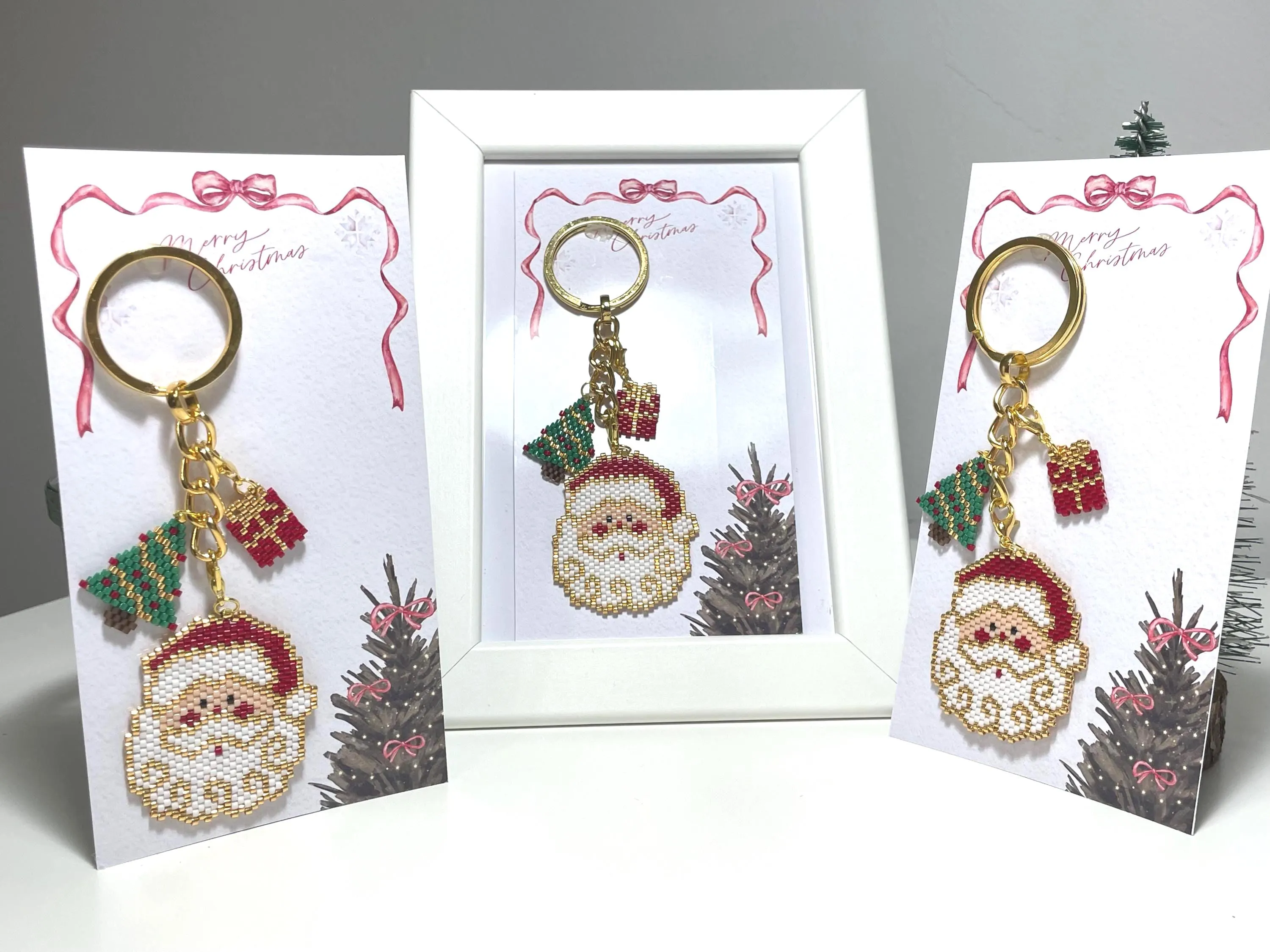 Bring holiday cheer wherever you go with this handmade beaded Christmas Santa & pine tree ornament! Perfect as a keychain, bag accessory, or meaningful gift for loved ones. The design features a Santa Claus, pine tree, and a matching mini gift ornament, all with festive red, green, gold, and white details.