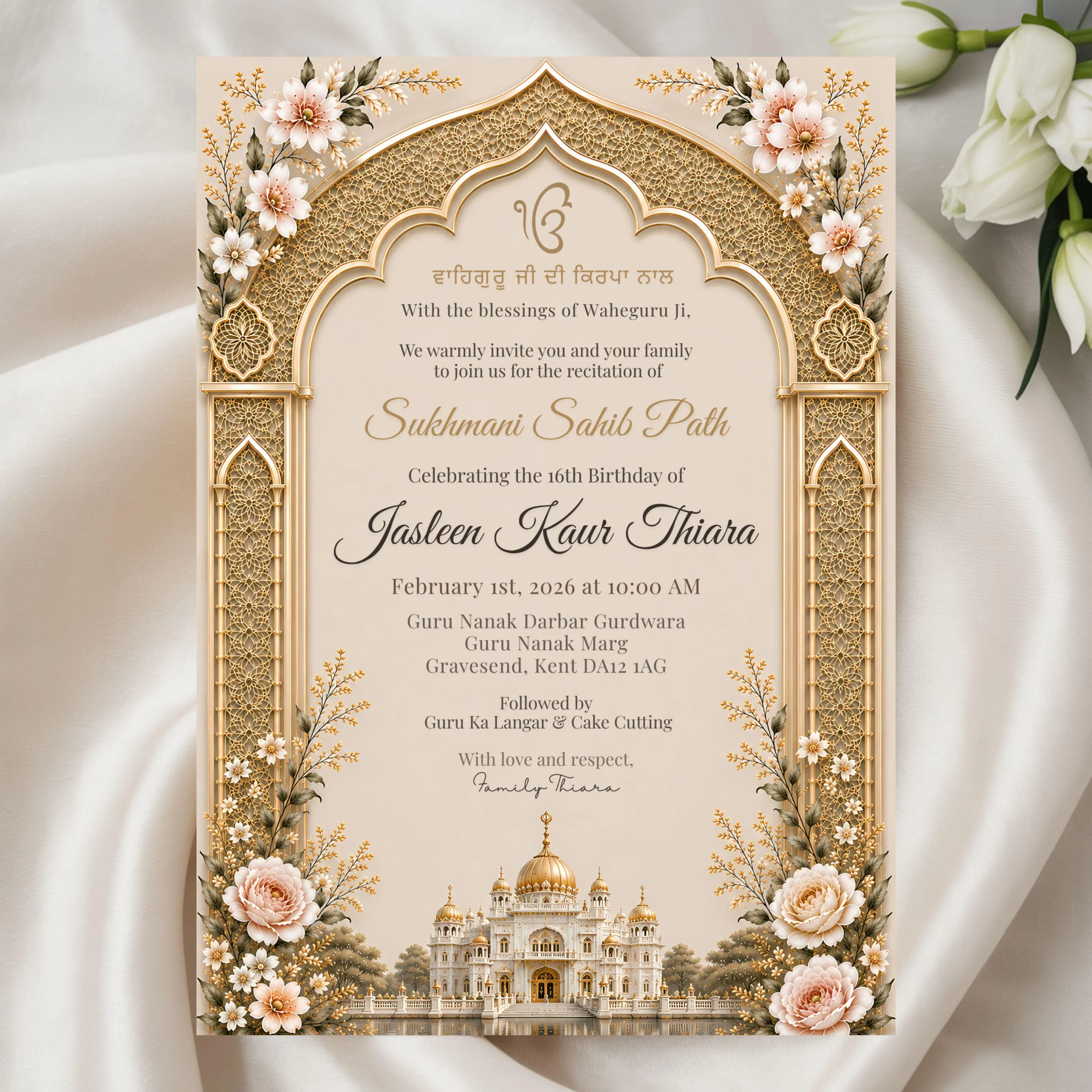 Luxury Sikh ceremony invitation with ornate golden arch displayed on soft ivory fabric with white floral accents.