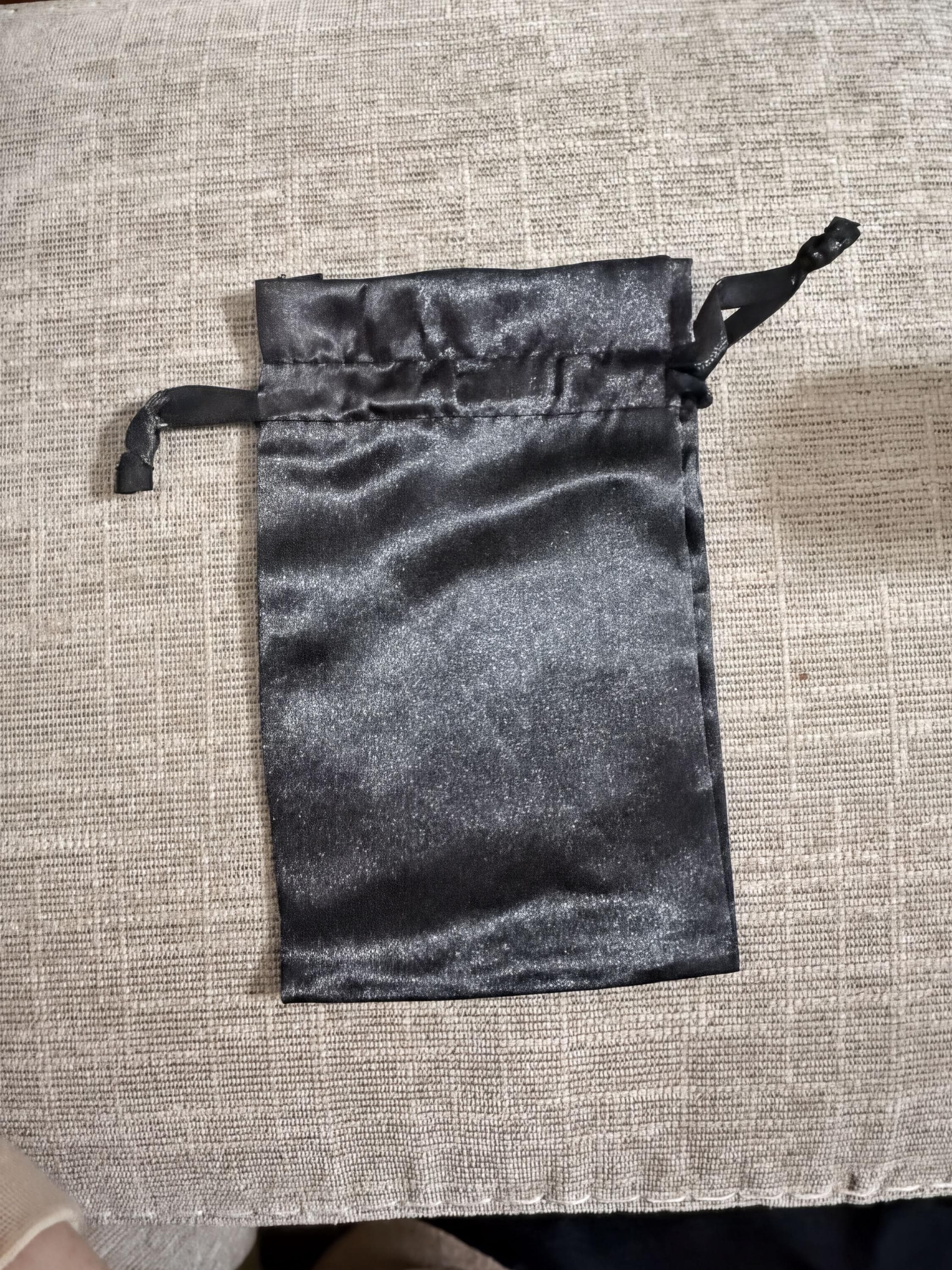 A black satin pouch or bag is placed on a textured fabric surface.