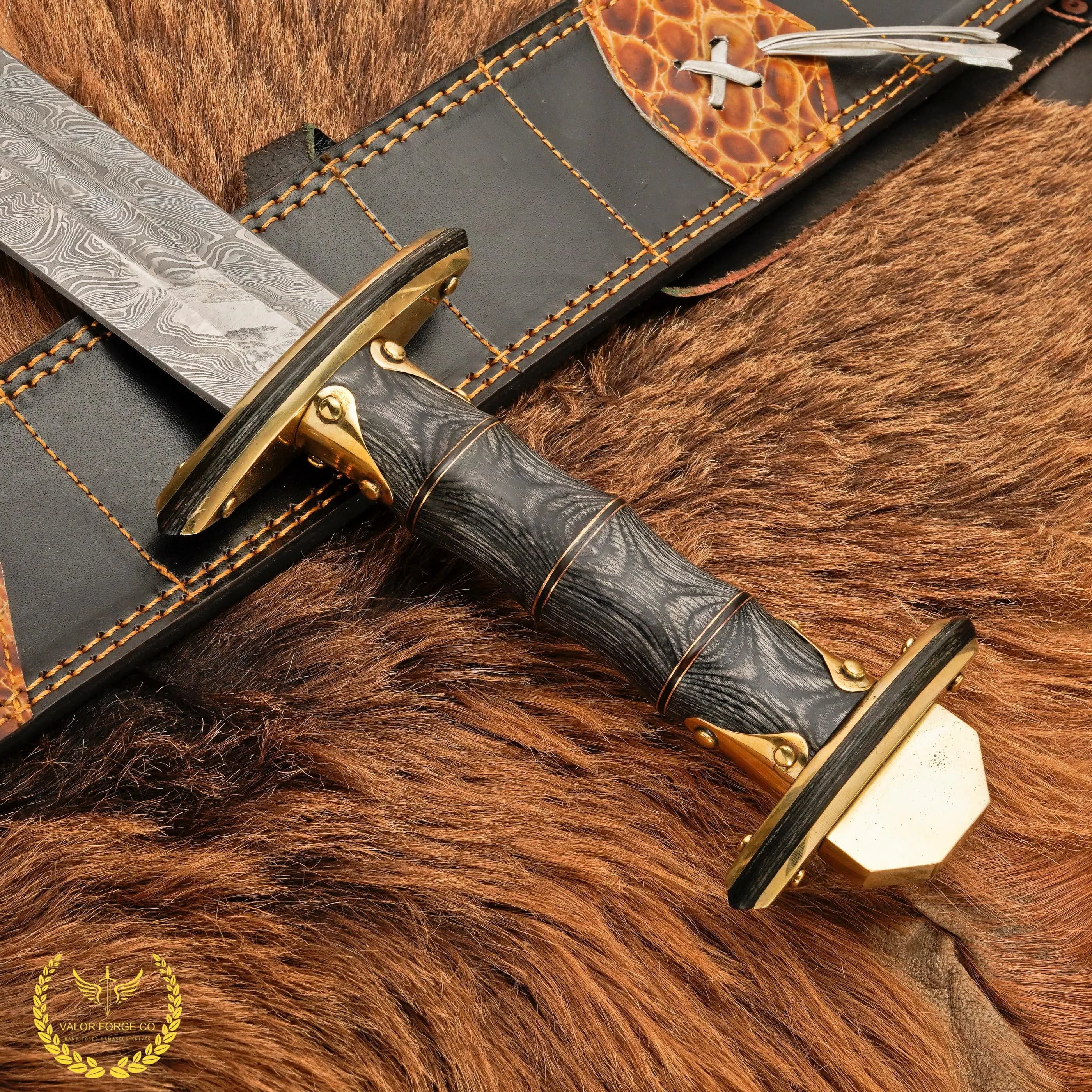 Angled close-up of the black grip and round gold-colored guard with the start of the patterned blade, next to the scabbard’s stitched edge and orange leather panel.