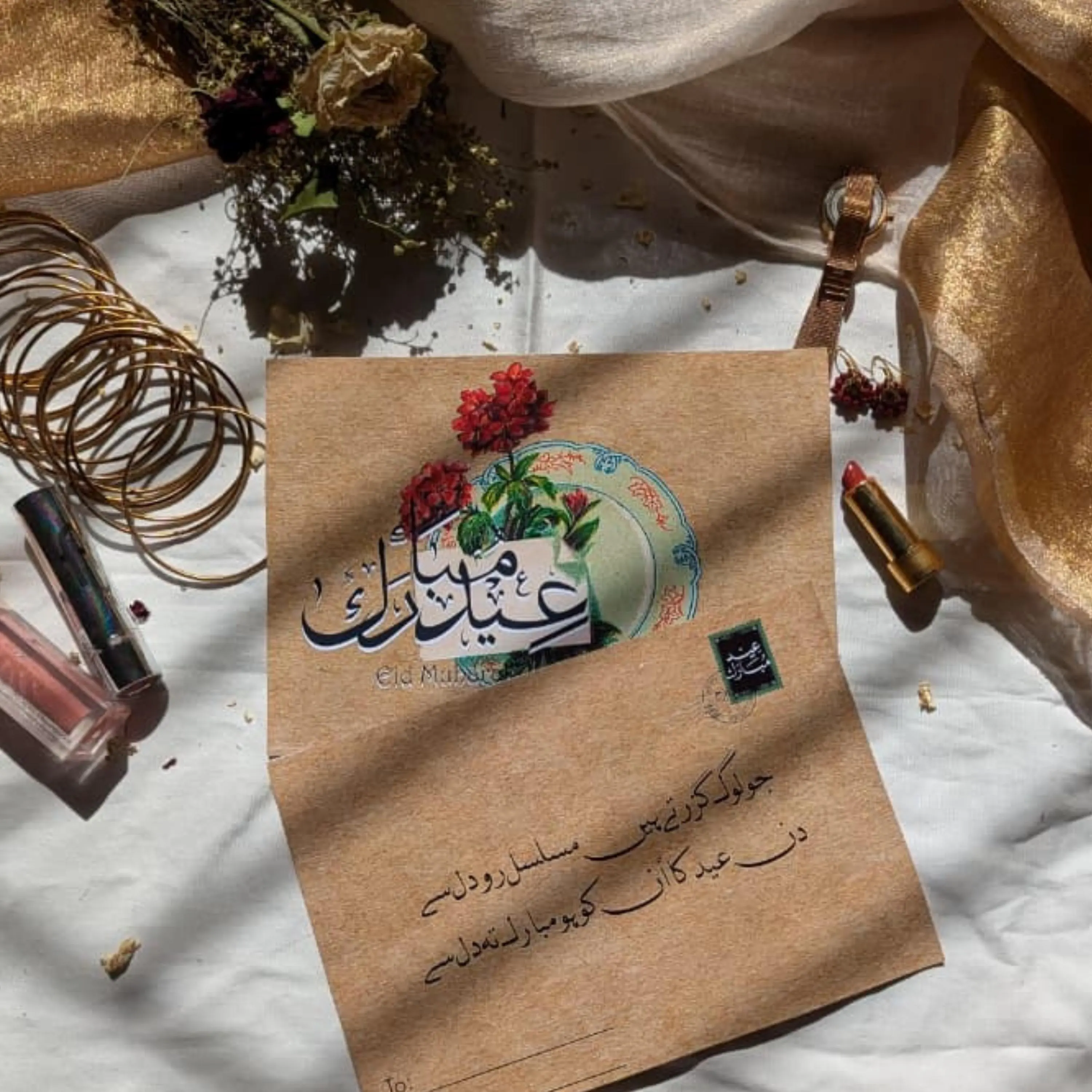 Close-up of Urdu Eid calligraphy card with blue pottery plate and crimson flowers