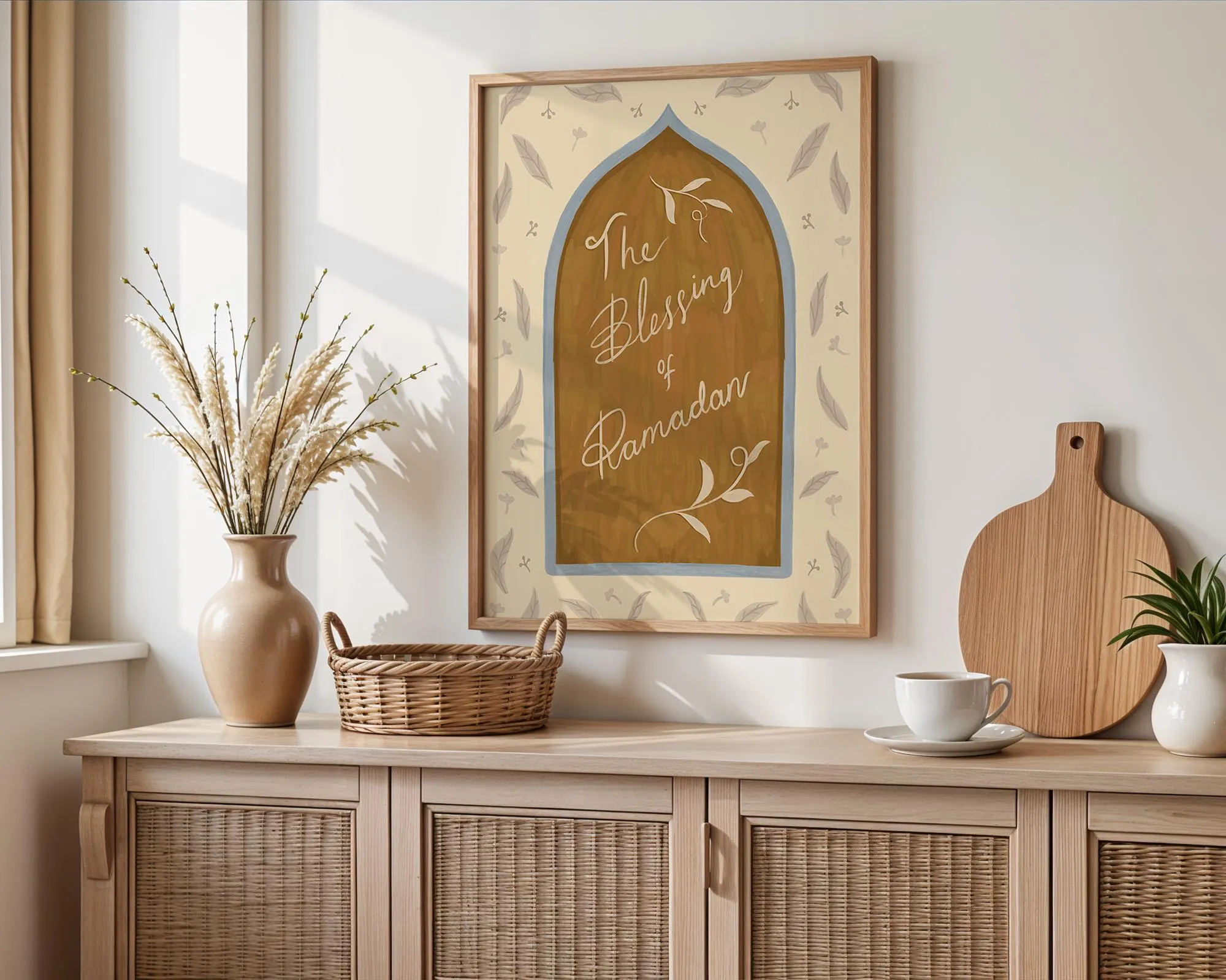 May include: A framed art print with the text "The Blessing of Ramadan". The artwork features a warm colour palette with a central arch design, surrounded by decorative elements. The print is displayed on a light-coloured wooden cabinet with other decorative items.