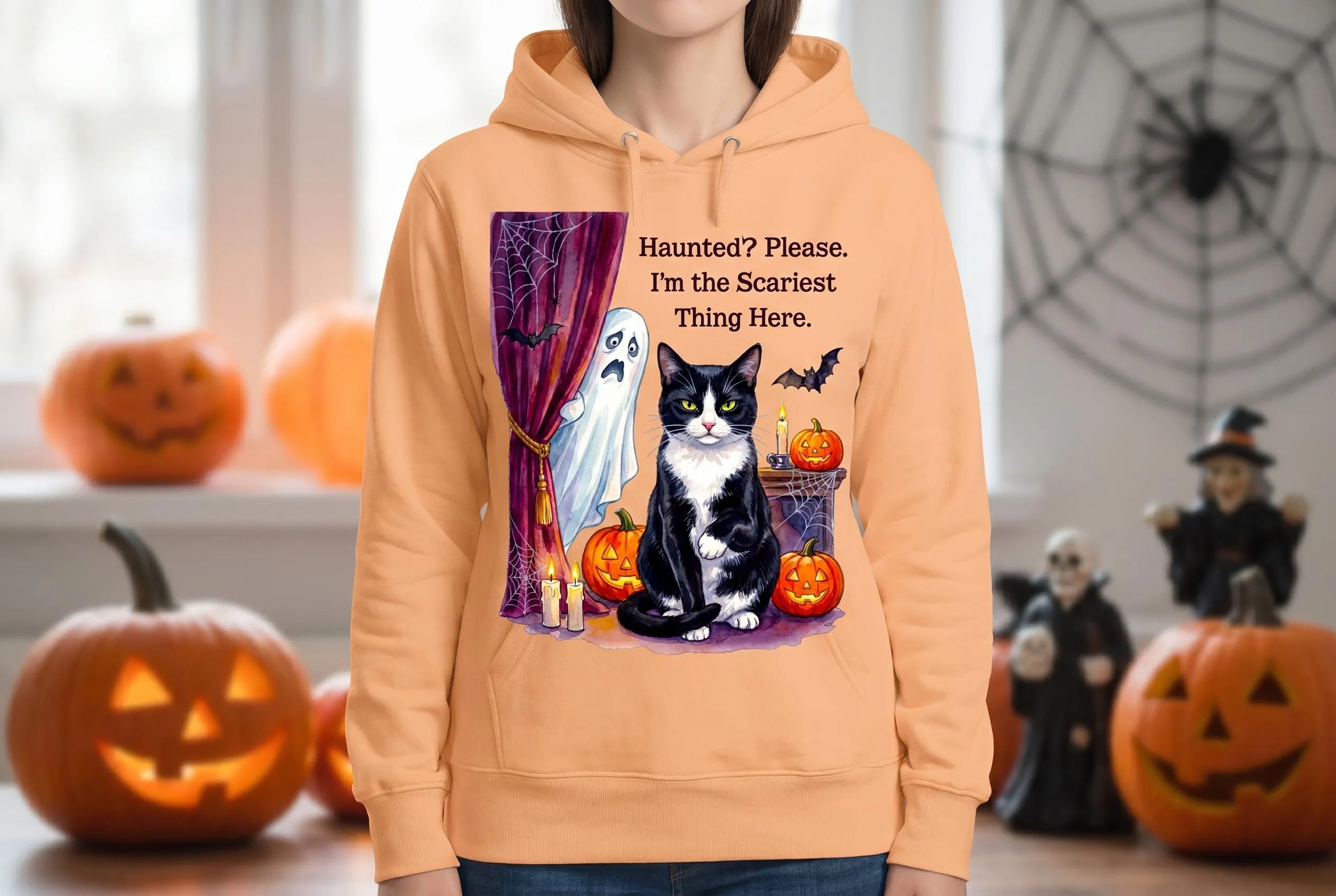 Ghost cat meme hoodie — tuxedo cat with yellow eyes, terrified ghost, Halloween pumpkins, candles, purple drapes, spiderweb, flying bats, "Haunted? Please. I'm the Scariest Thing Here" quote. Creepy cat Halloween trending shirt PNG.