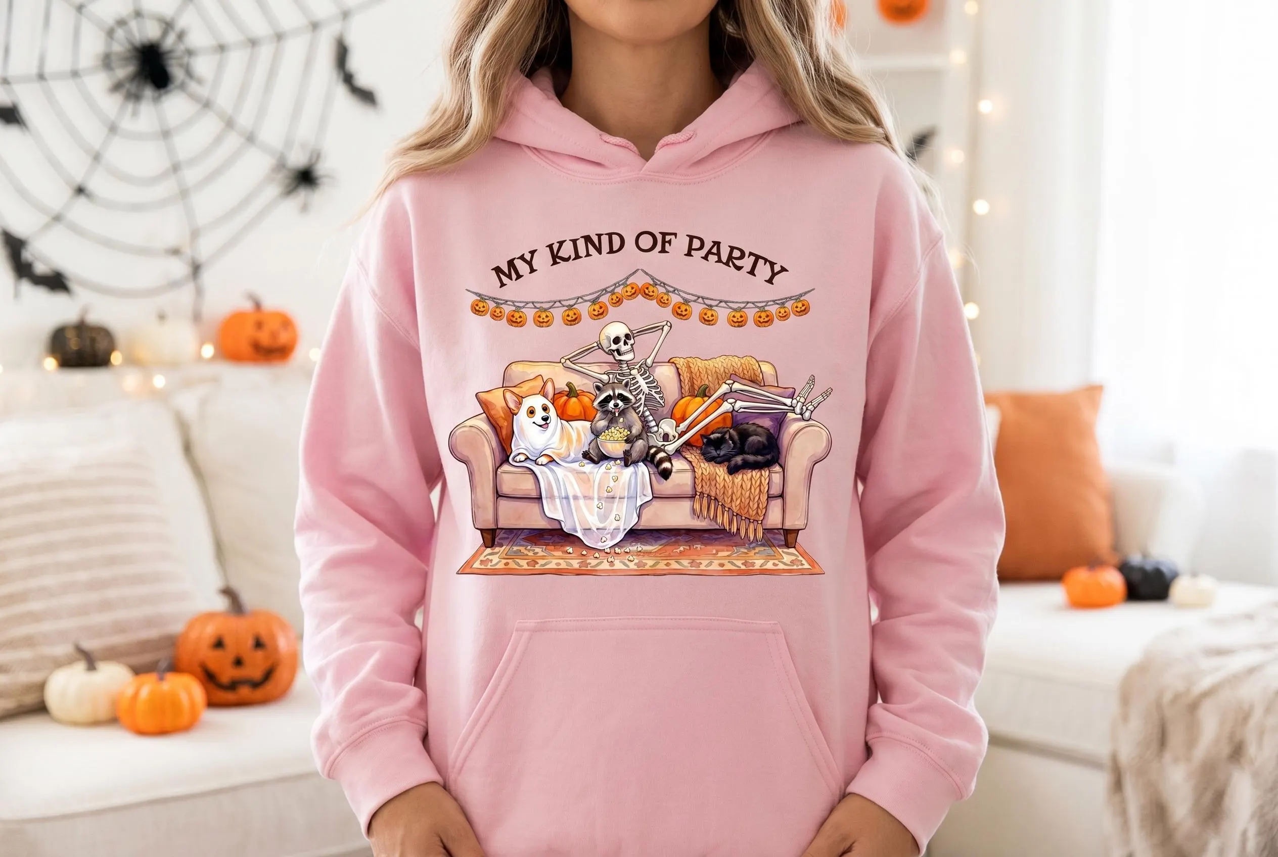 Halloween PNG on hoodie — "MY KIND OF PARTY" text with skeleton relaxing on couch with corgi dog, raccoon eating popcorn, black cat, orange pumpkin, blankets, pillows, jack-o-lantern garland. Introvert shirt funny Halloween meme design.
